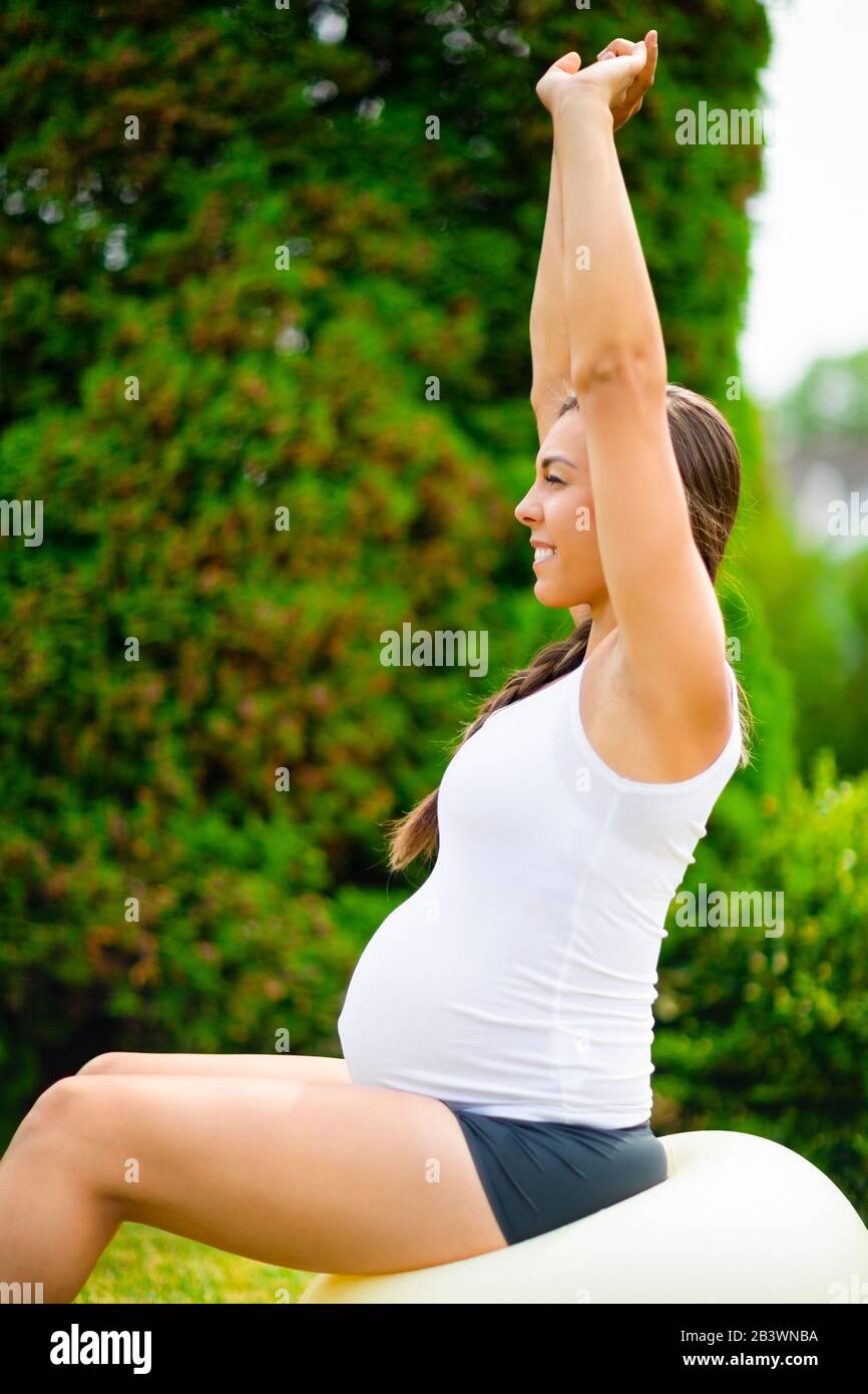 Schwangere Frau Streckt Die Hände, Während Sie Auf Dem Yoga-Ball Sitzt Stockfoto
