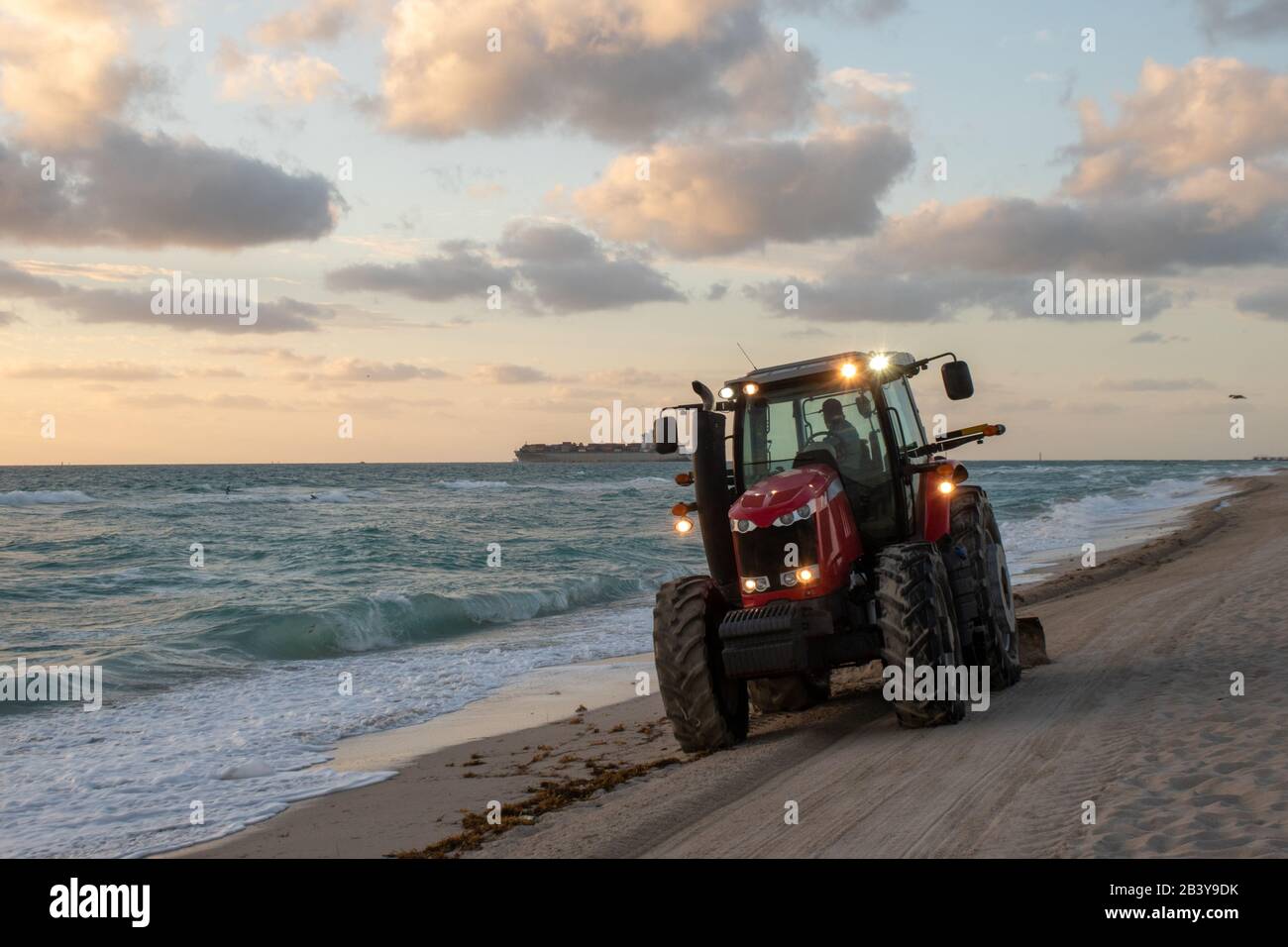 Tractor, der den Strand an einem Kühlen Morgen Sonnenaufgang in Miami South Beach, Florida, säubert. Wind brachte einige hohe Wellen. Stockfoto