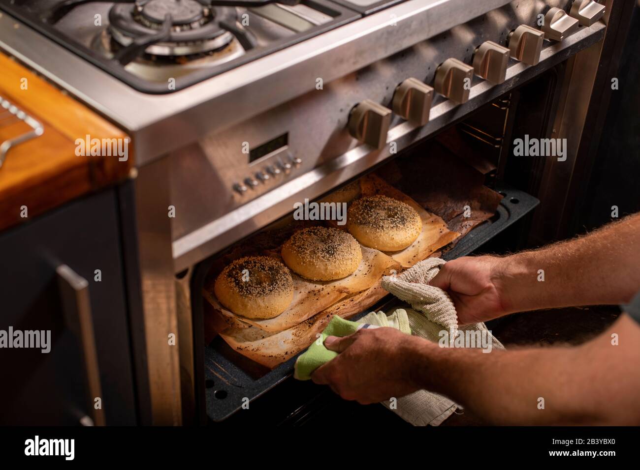 Koch greift mit zwei Händen, um frisch gebackene Bagels aus einem heißen Ofen zu ziehen Stockfoto
