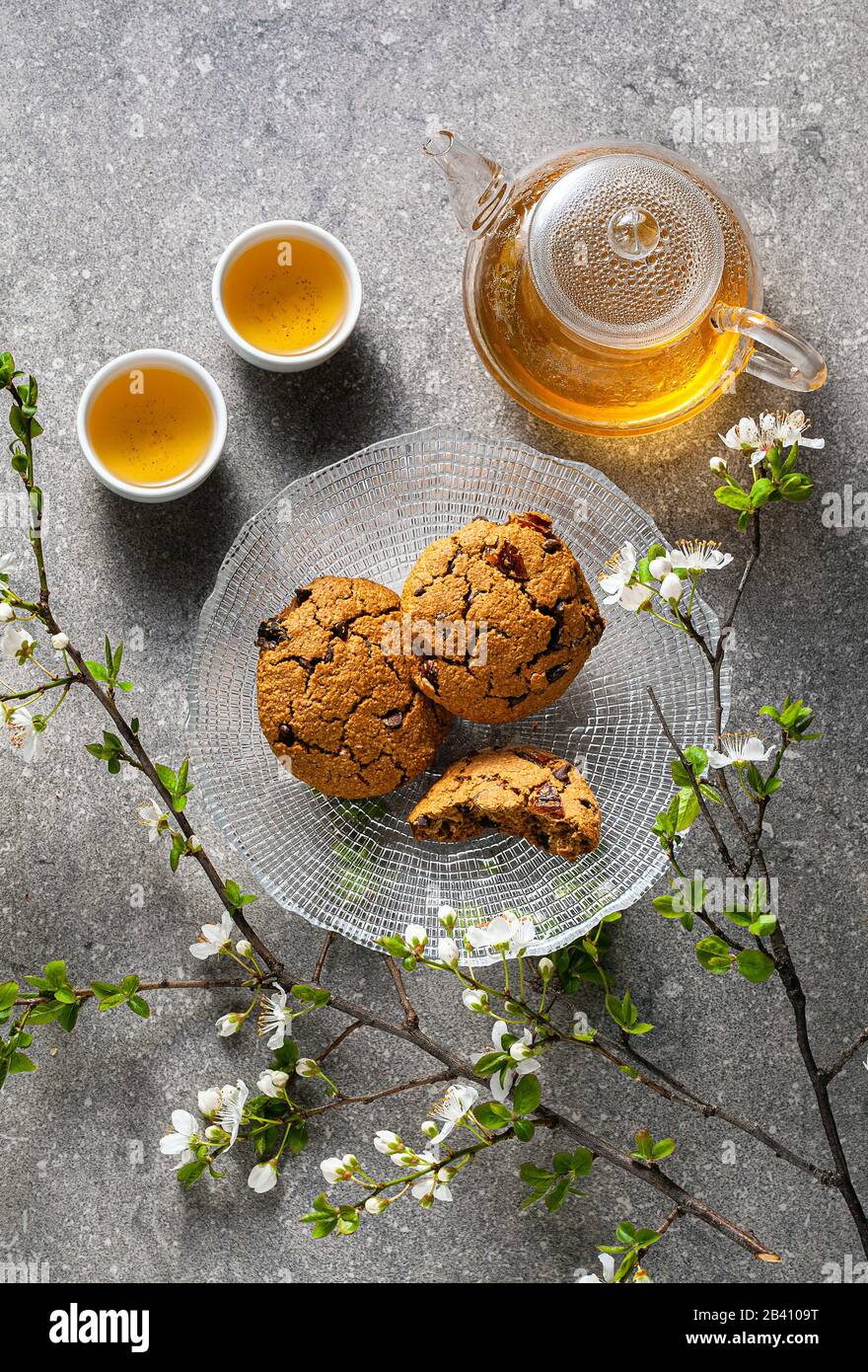 Hausgemachte Haferflocken auf einem Tisch mit Ästen eines blühenden Baums und grünem Tee in einer Glaskanne. Stockfoto