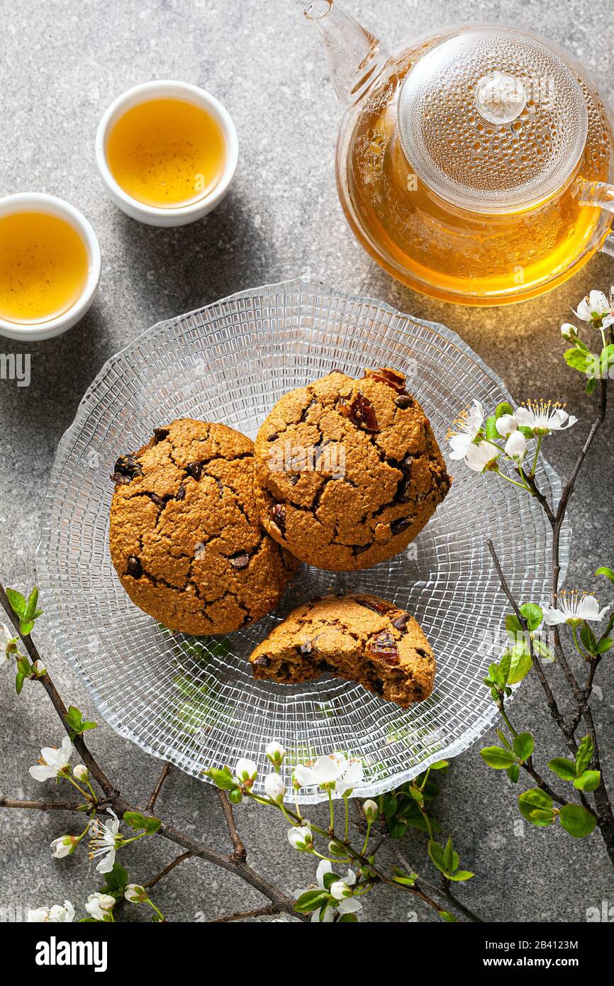 Hausgemachte Haferflocken auf einem Tisch mit Ästen eines blühenden Baums und grünem Tee in einer Glaskanne. Stockfoto