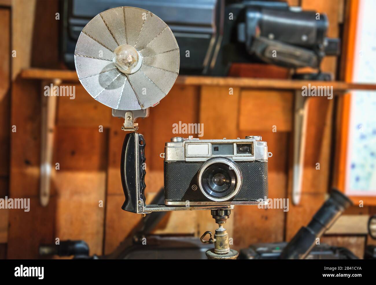 Alte Kamera und faltbarer Reflektor der Taschenlampe auf Stativ, auf isoliertem verschwommenem Hintergrund mit Beschneidungspfad. Stockfoto
