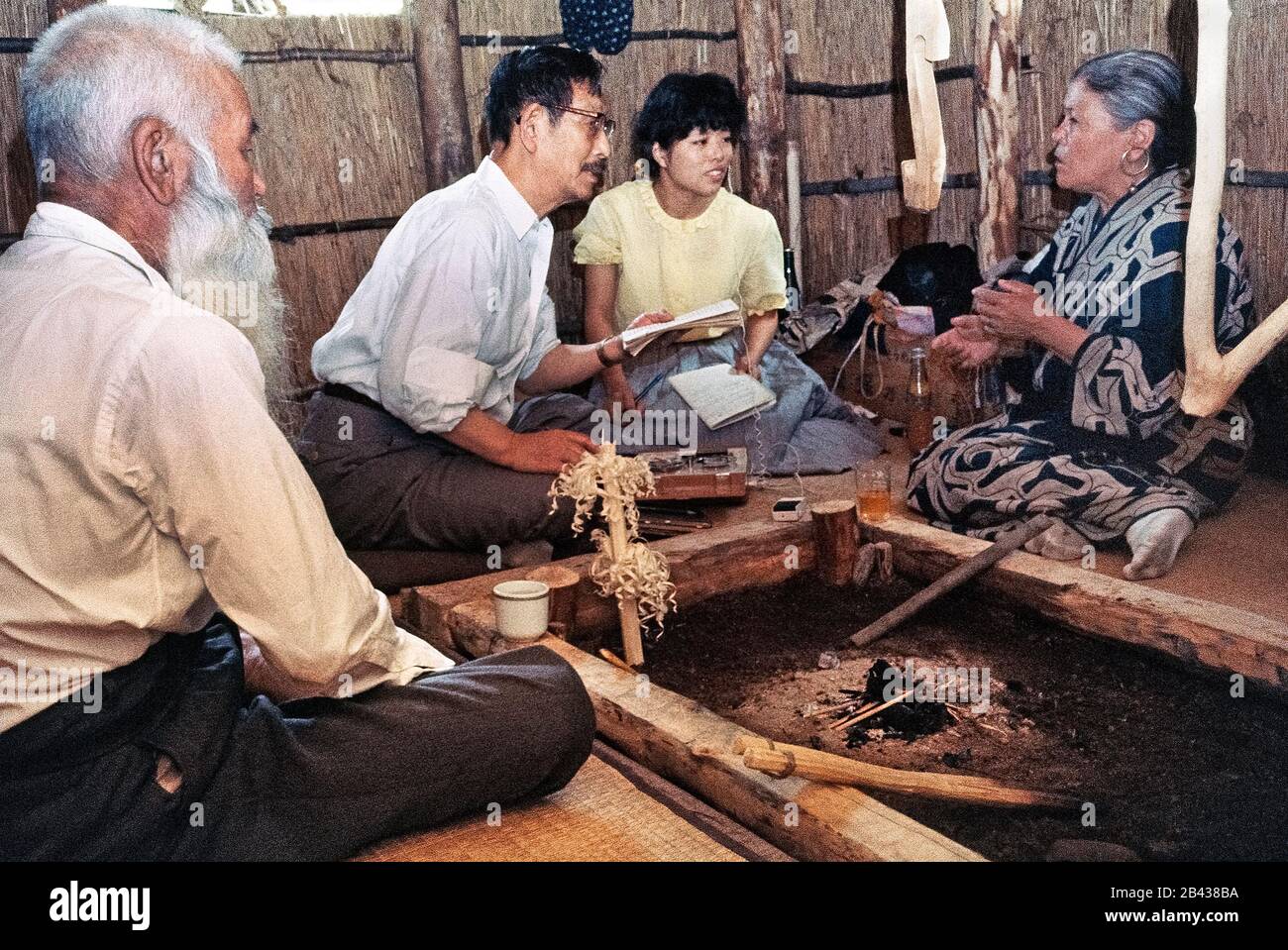 Der japanische Sprachwissenschaftler Professor Kyosuke Kindaichi und sein weibliches Assistenteninterview eine ältere Ainu-Frau in traditionellem Kleid, als ihr bärtiger Ehemann ihre Geschichten in ihrer Heimat auf der Insel Hokkaido im Norden Japans hört. Sie waren zwei von nur 300 reinblütigen Ainu (ausgesprochen i-noo), die noch lebten, als diese historische Fotografie 1962 aufgenommen wurde. Seit dieser Zeit haben sich die Ainu in die japanische Gesellschaft eingenistet und ihre uralte Lebensweise wird heute nur noch in besonderen Touristendörfern erblickt. Die Ainu wurden 2008 offiziell als Ureinwohner Japans anerkannt. Stockfoto