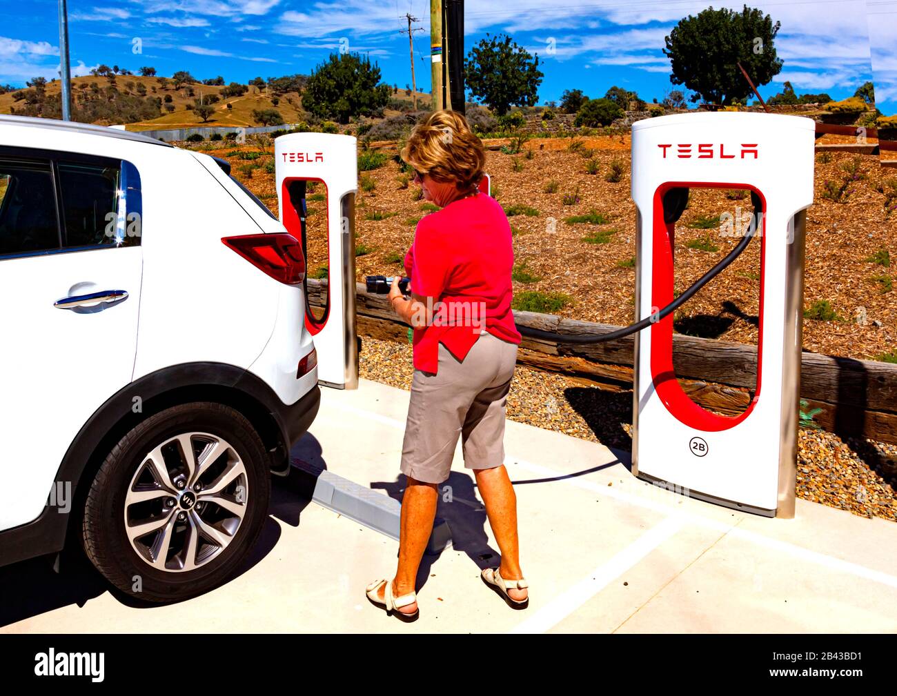 Weibliche Touristen, die sich vorbereiten, ihr Auto bei Tesla Ladung aufzuladen Bahnhof in der Nähe von Gundagai am Hume Highway im australischen Bundesstaat New South Wales Stockfoto