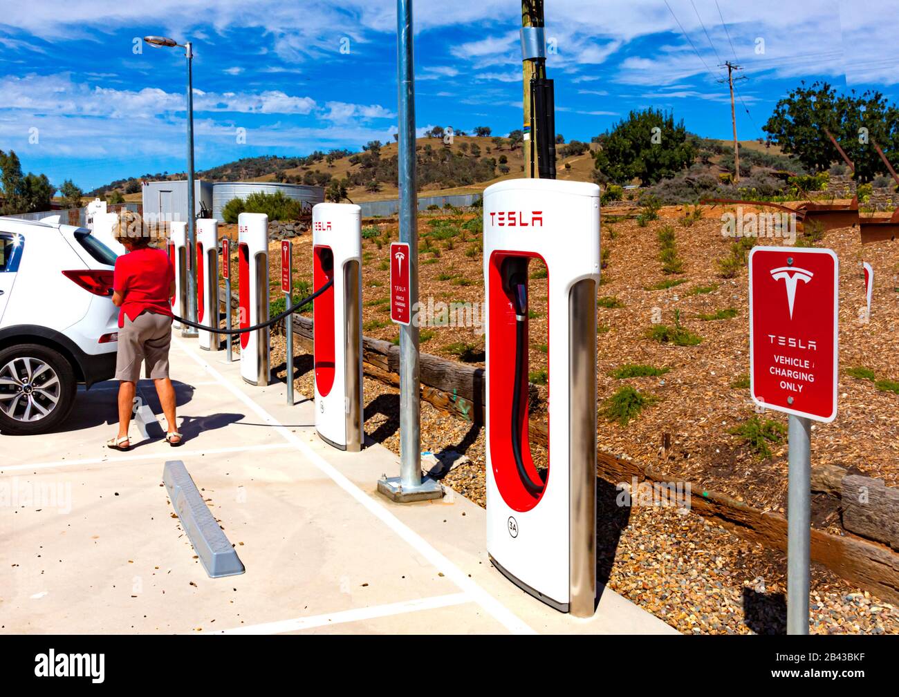 Frau Tourist lädt ihr Fahrzeug an der Tesla-Ladestation Einheit in der Nähe von Gundagai auf dem Hume Highway zwischen Sydney und Melbourne in Australien Stockfoto