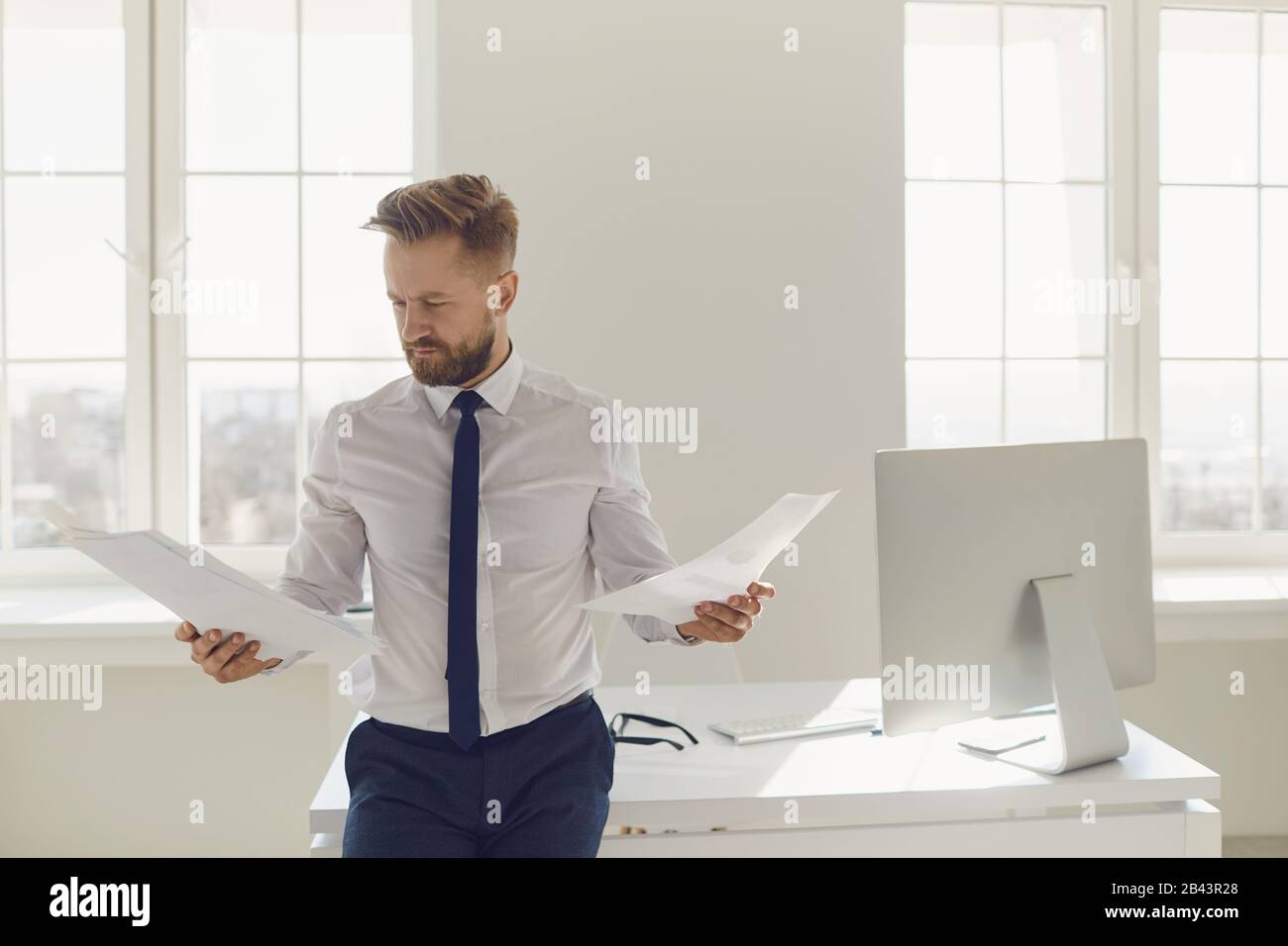 Blonder Geschäftsmann mit Papierdokumenten in den Händen, die im Büro arbeiten Stockfoto
