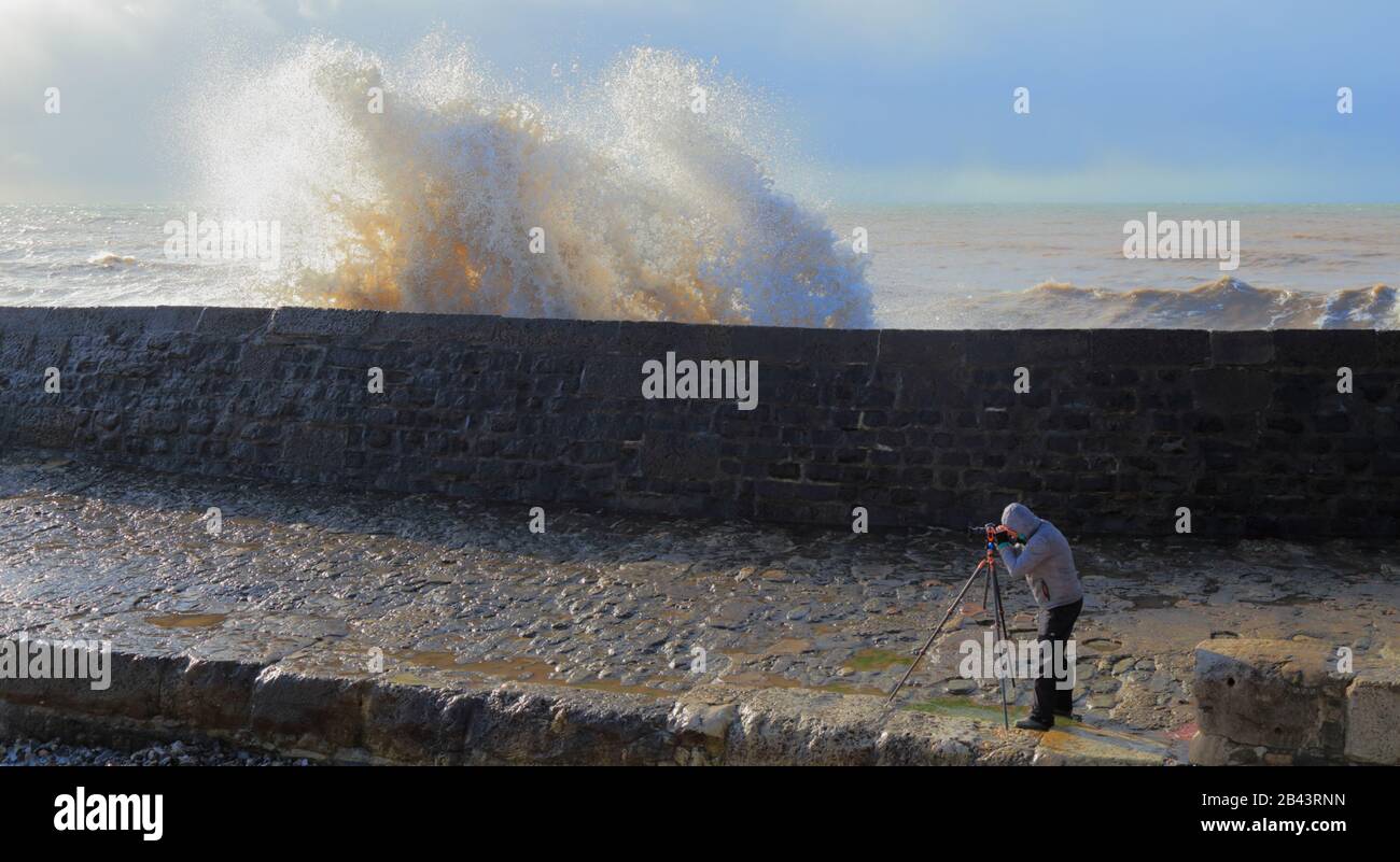 Fotograf, der auf Dem Cobb in Lyme Regis, Dorset, ein Bild vom Wellenspritzen macht Stockfoto