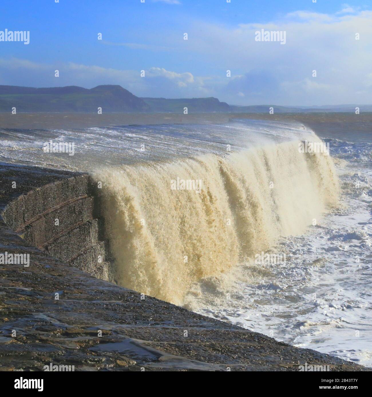 Große Welle, die bei Flut und starkem Wind auf Den Cobb spritzt Stockfoto