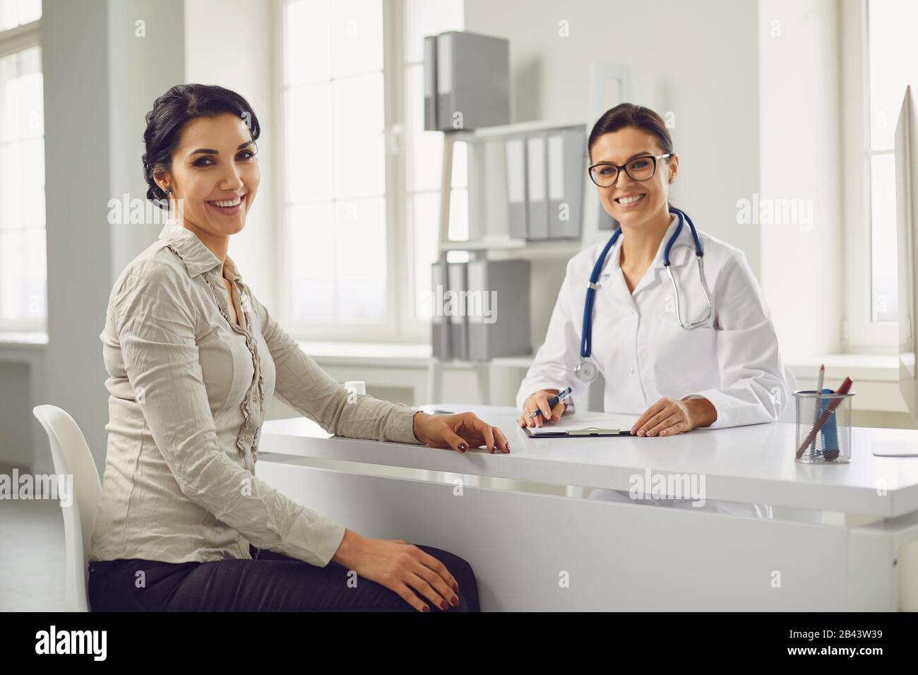 Lächelnde Patientin nach Rücksprache mit einem am Tisch sitzenden Frauenarzt in der Büroklinik. Stockfoto