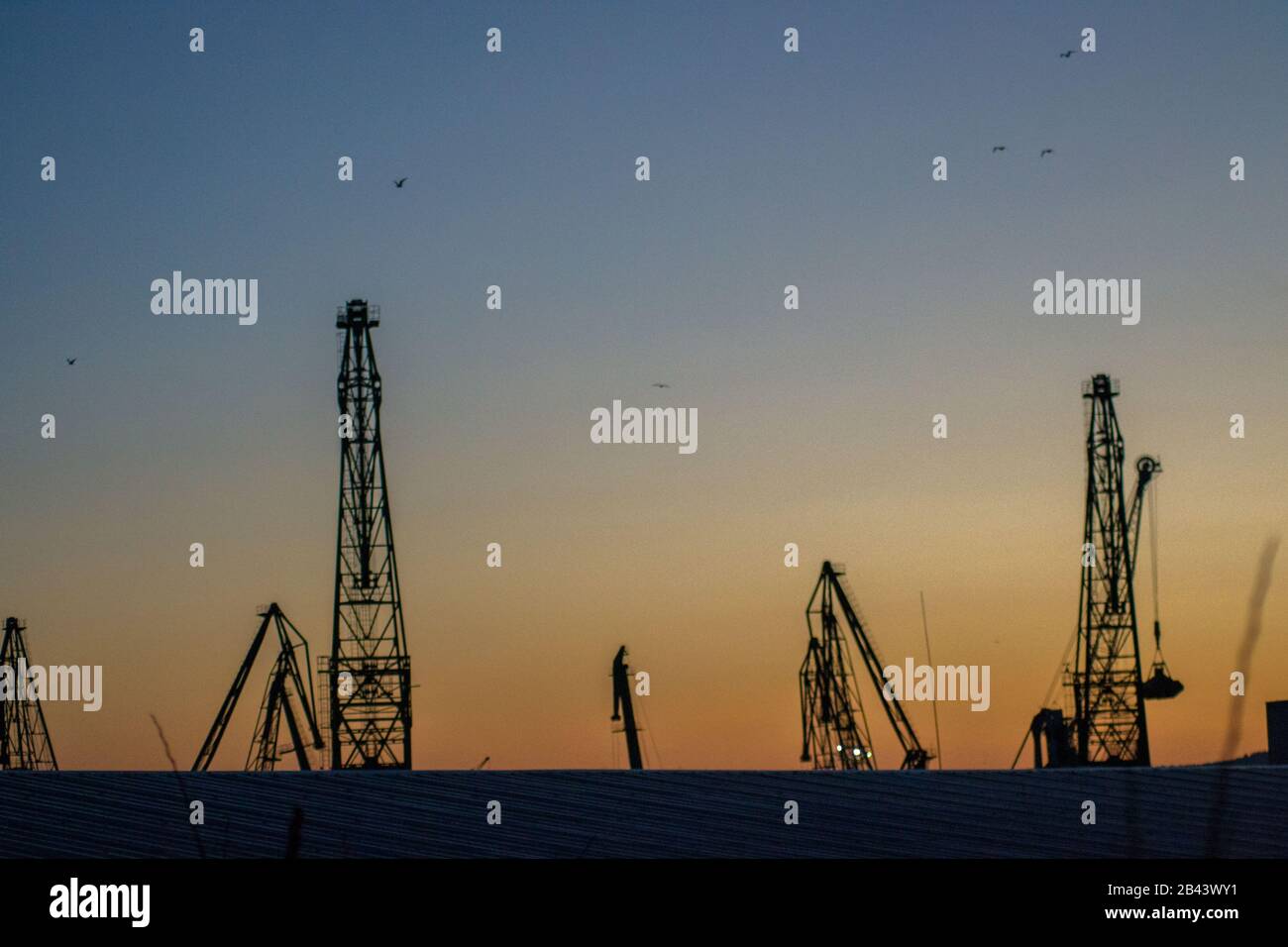 Cargo Krane Silhouetten gegen den dramatischen blauen und orangen Sonnenuntergang Himmel, Warna, Bulgarien, Kran im Hafen Stockfoto