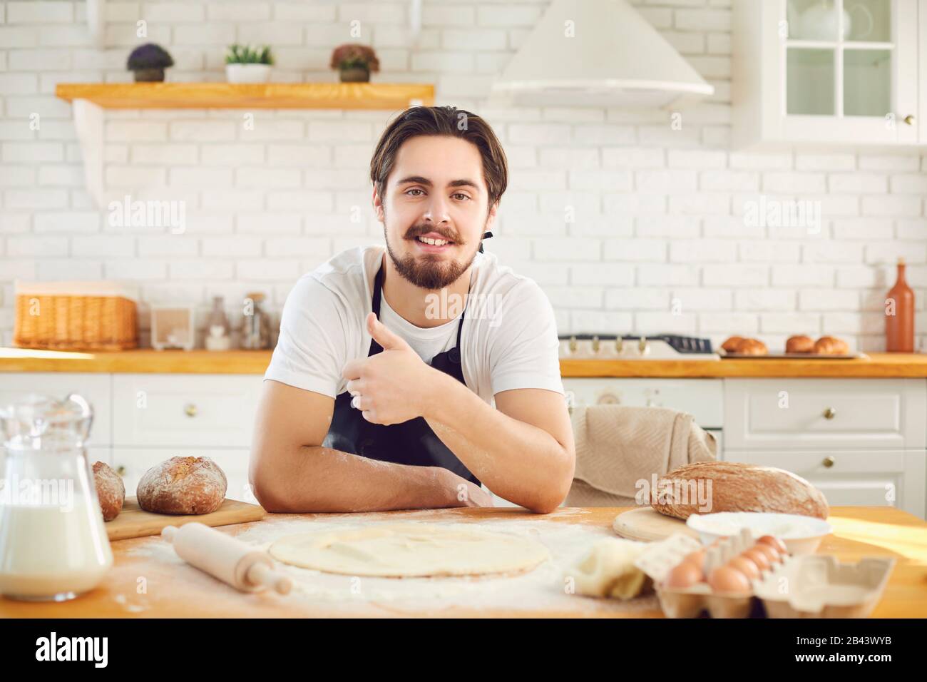 Bärtiger bärtiger Mann, der vor dem Hintergrund von frischem Brot in der Backküche lächelte Stockfoto