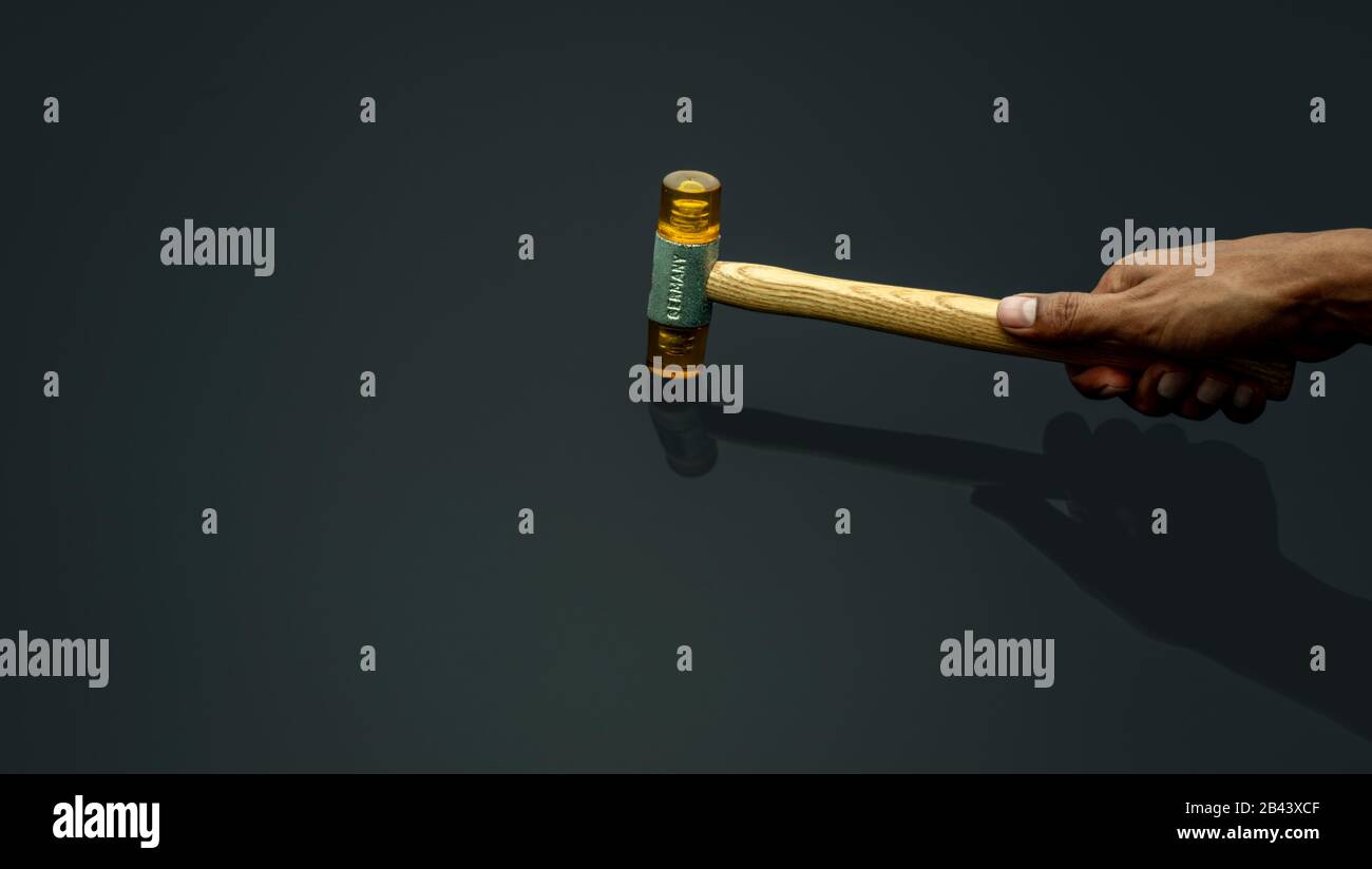 Hand des Mannes, der Kunststoffhammer isoliert auf dunklem Hintergrund hält. Holzgriff aus Kunststoffhammer für die Hand des männlichen Arbeiters. Hammerkopf aus weichem und Stockfoto