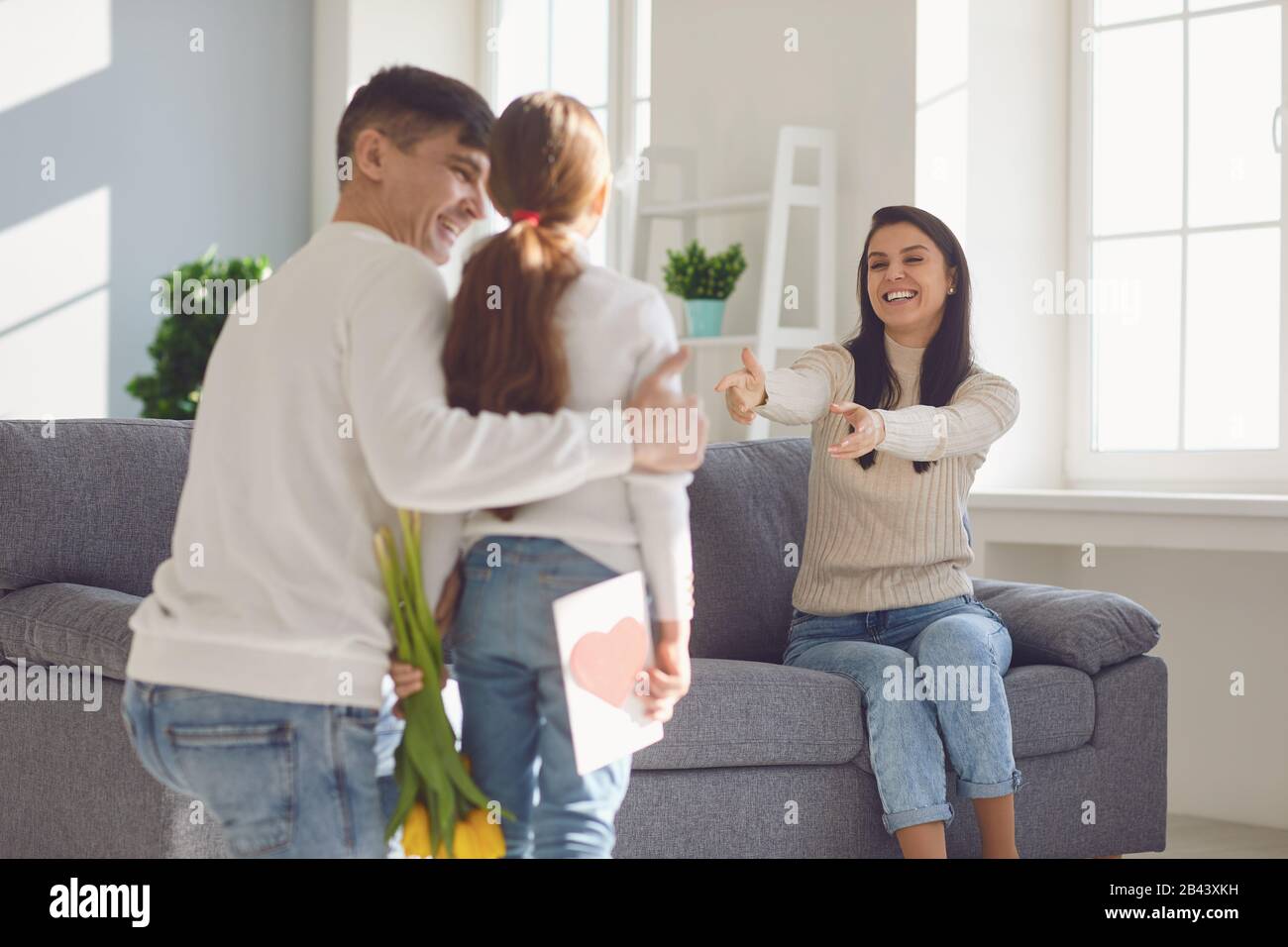 Glücklicher Muttertag. Vater und Tochter des Babys gratulieren Mutter mit Blumen und einer Postkarte in einem Zimmer Stockfoto