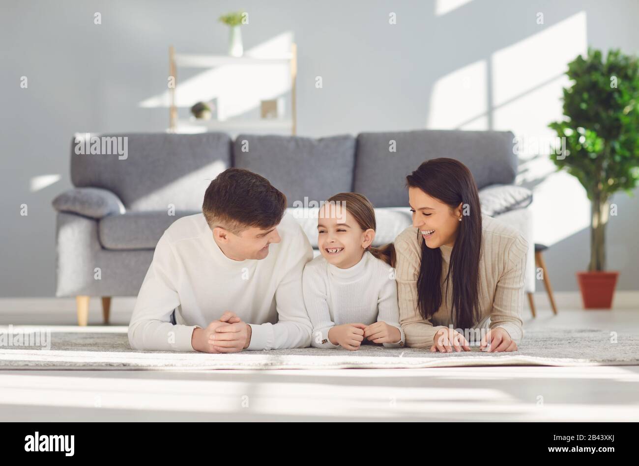 Fröhliche lächelnde Familie umarmt, während sie zu Hause auf dem Boden im Zimmer liegt. C Stockfoto