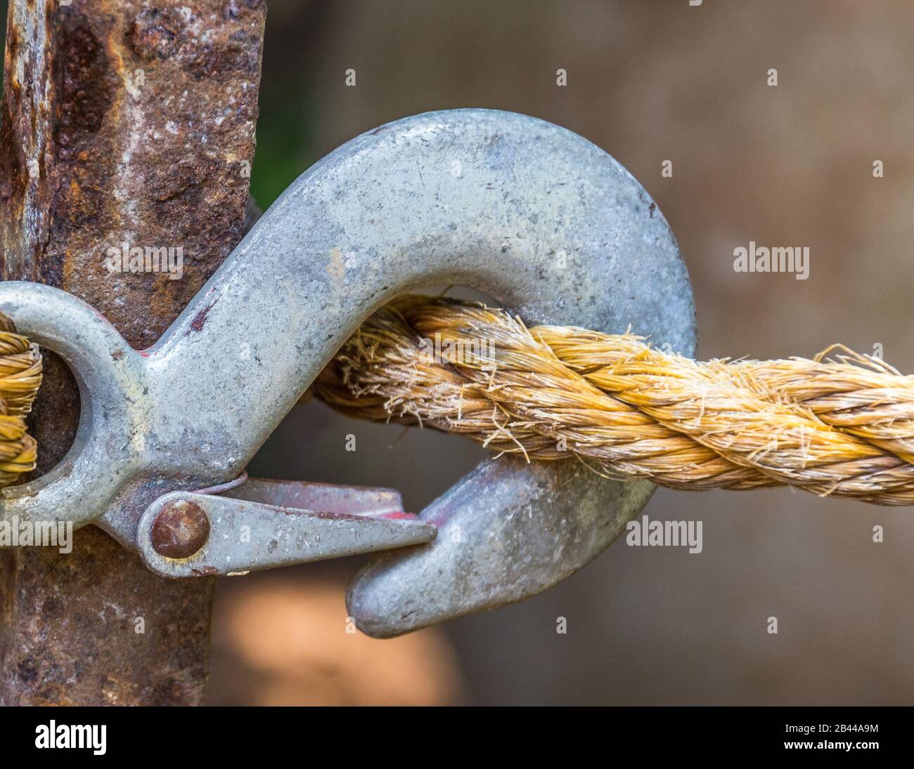 Metallverschluss an einem dicken, isolierten Seil, das um ein verrostetes Metallpfahl in horizontaler Form geschleift ist Stockfoto