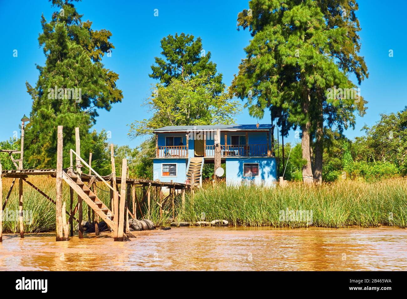 Üppige Vegetation, traditionelles Holzhaus am Holzsteg und orangefarbenes Lehmwasser. Tigra-Delta in Argentinien, Flusssystem des Parana-Delta-Nordens ab Ca Stockfoto