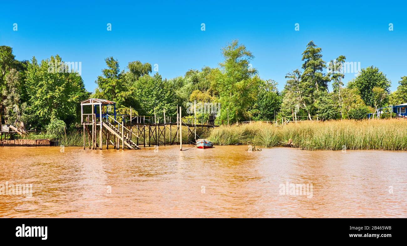 Üppige Vegetation, Fischer bootern am Holzsteg und orangefarbenem Lehmwasser. Tigra Delta in Argentinien, Flusssystem des Parana Delta Nord von der Hauptstadt Bu Stockfoto