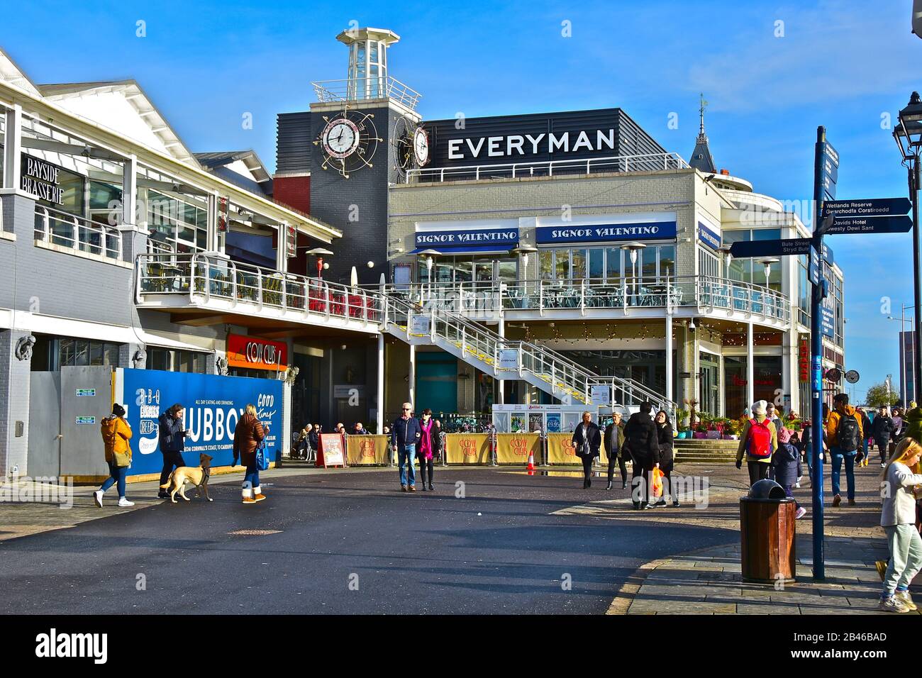 Die Menschen schlendern im Winter unter der Sonne unter den vielen Bars, Geschäften und Restaurants im Mermaid Quay in Cardiff Bay. Die Gegend ist bekannt als "Tacoma-Platz". Stockfoto