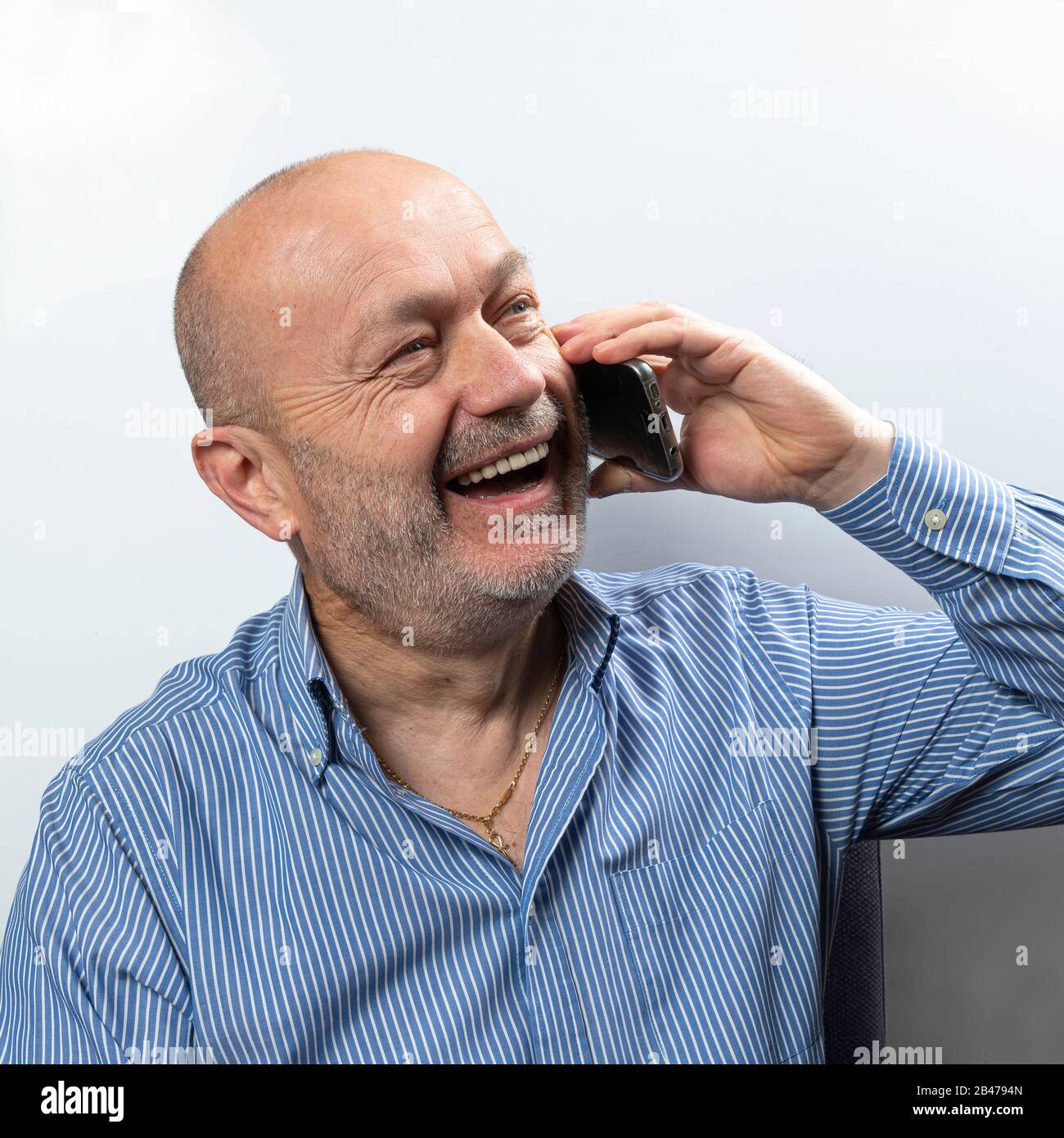 Ein Mann mittleren Alters lacht während eines Handy-Gesprächs Stockfoto