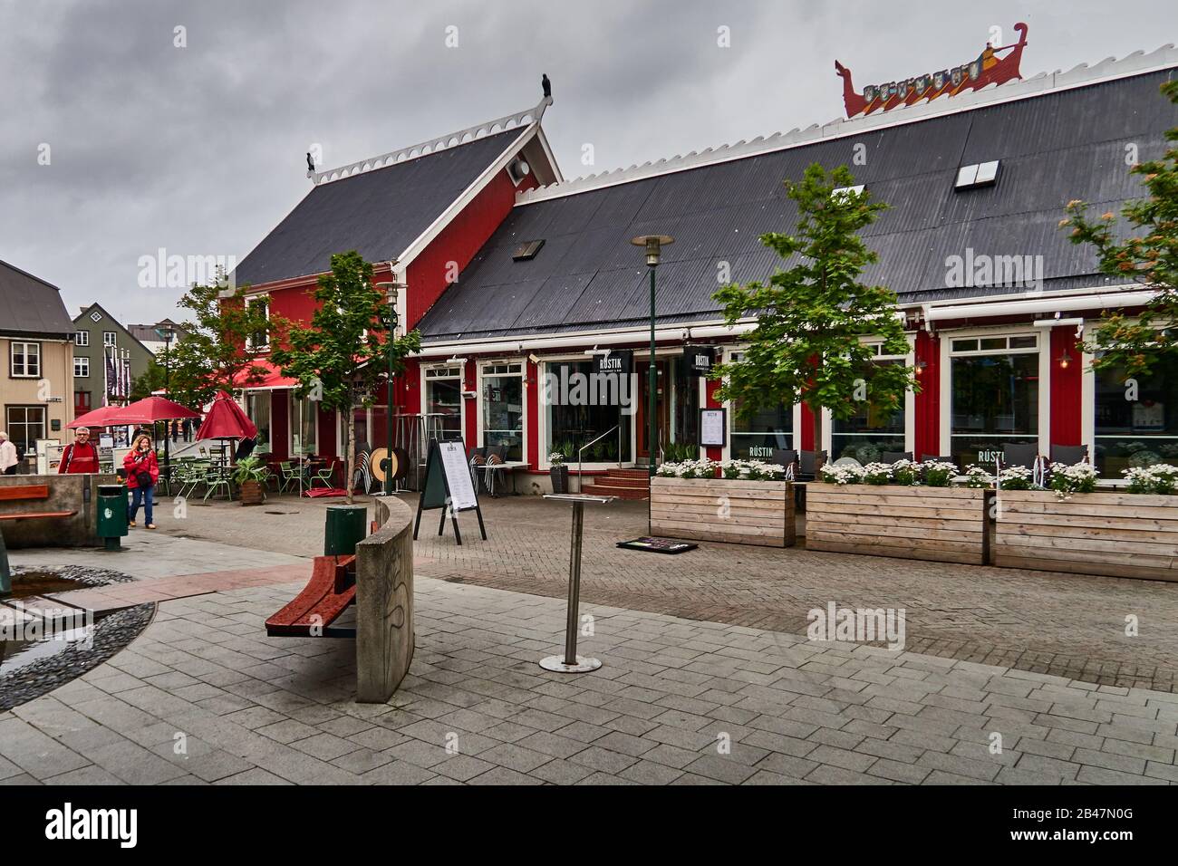 Europa, Reykjavik, Island., Ingolfstorg-Platz, rotes Langhaus mit einem Langschiff und 4 Statuen von Falken, Geschäften und Restaurants während eines regnerischen Tages im Sommer Stockfoto