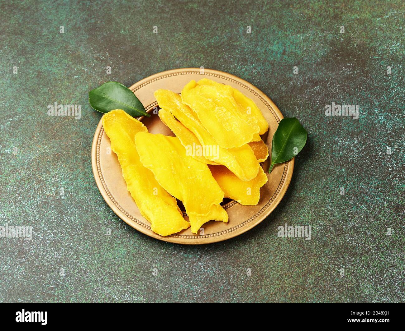 Getrocknete Mango-Früchte mit frischen Blättern auf grünem Grund. Mango in gelber Scheiben. Stockfoto