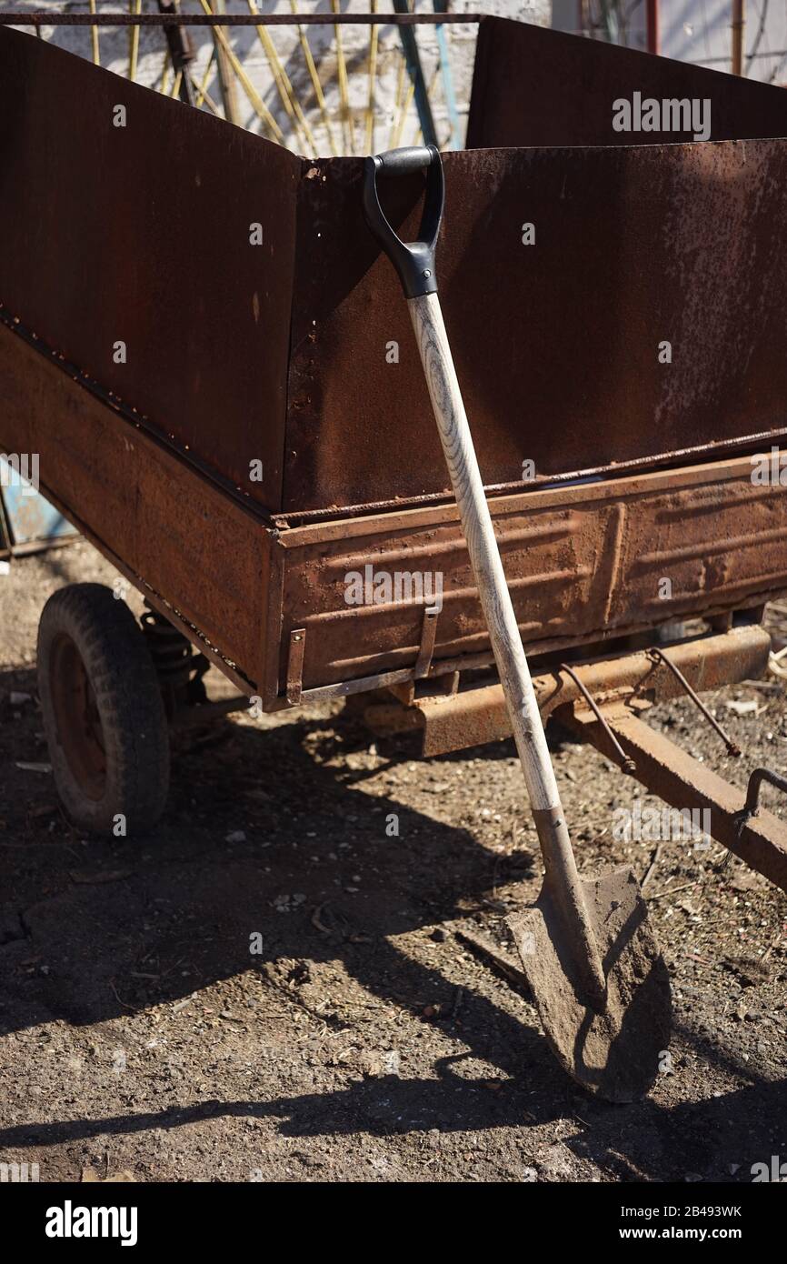 Eine schmutzige Schaufel steht an einem rostigen Anhänger in einem ländlichen Hof. Stockfoto