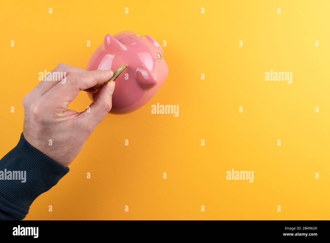 Geld sparen und Gewinnkonzept machen, Blick von oben auf das Einfügen goldener Münzen in pinke Piggy-Bank vor orangefarbenem Hintergrund Stockfoto
