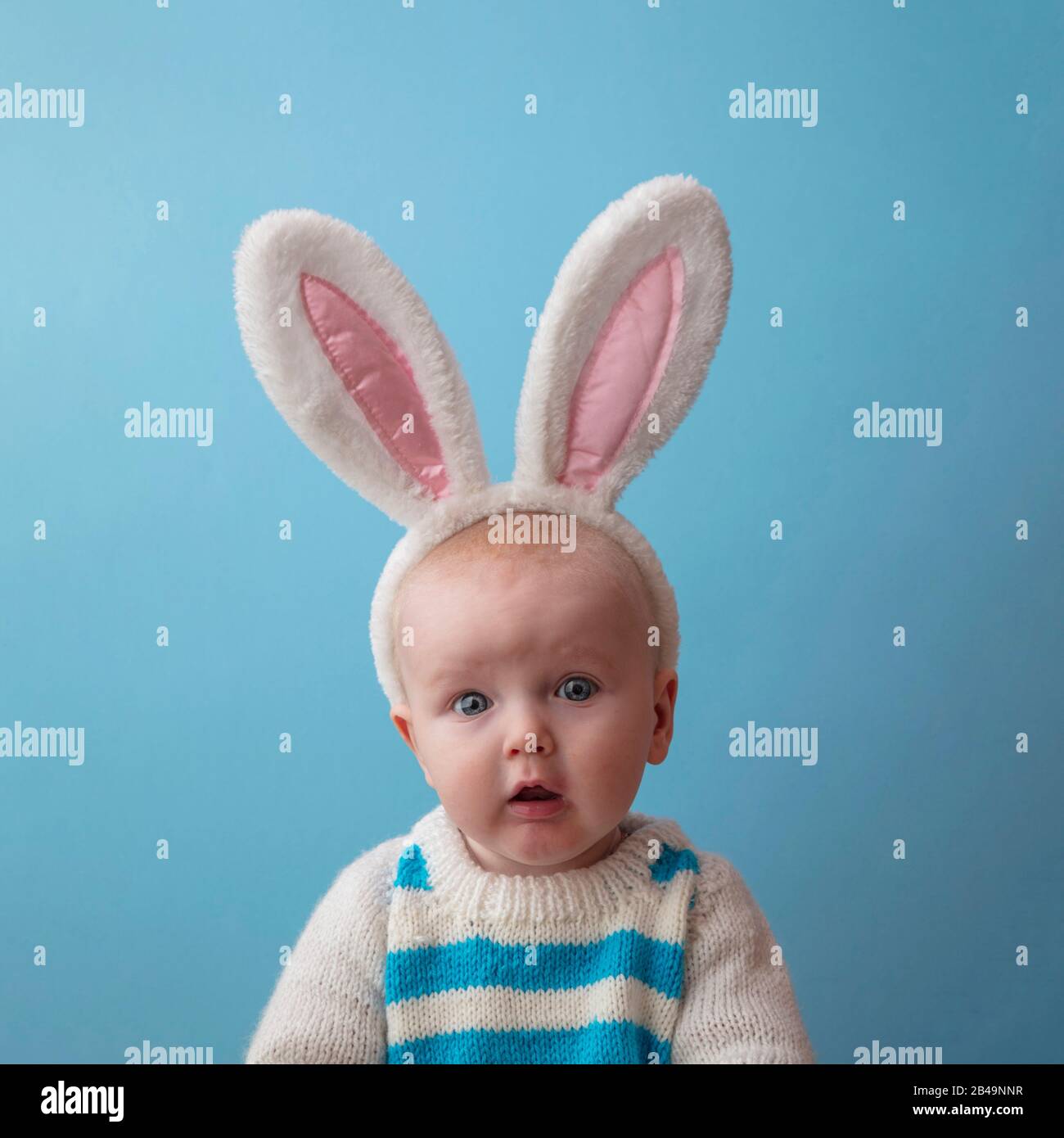 Traurig aussehendes Baby mit weißen osterhasen vor blauem Hintergrund Stockfoto