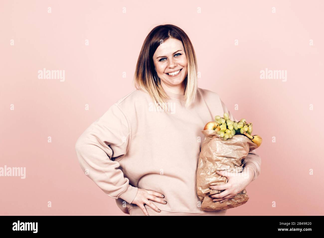 Attraktive positive Frau mit einem Papierbeutel voller Früchte - gesundes Essen und Lifestyle-Konzept Stockfoto