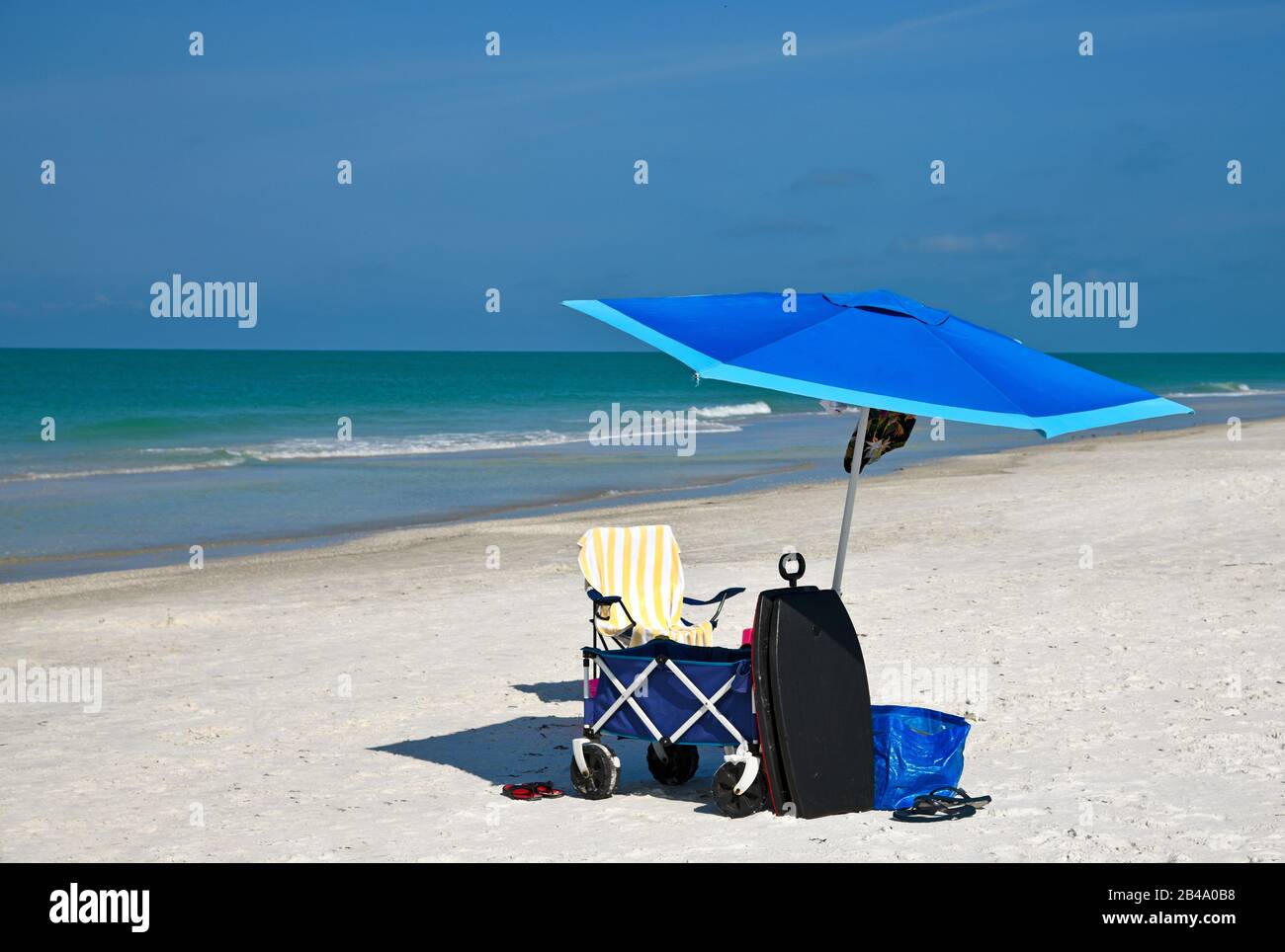 Ein Sonnenschirm und ein Stuhl mit verschiedenen Strandartikeln für einen Tag am Strand Stockfoto