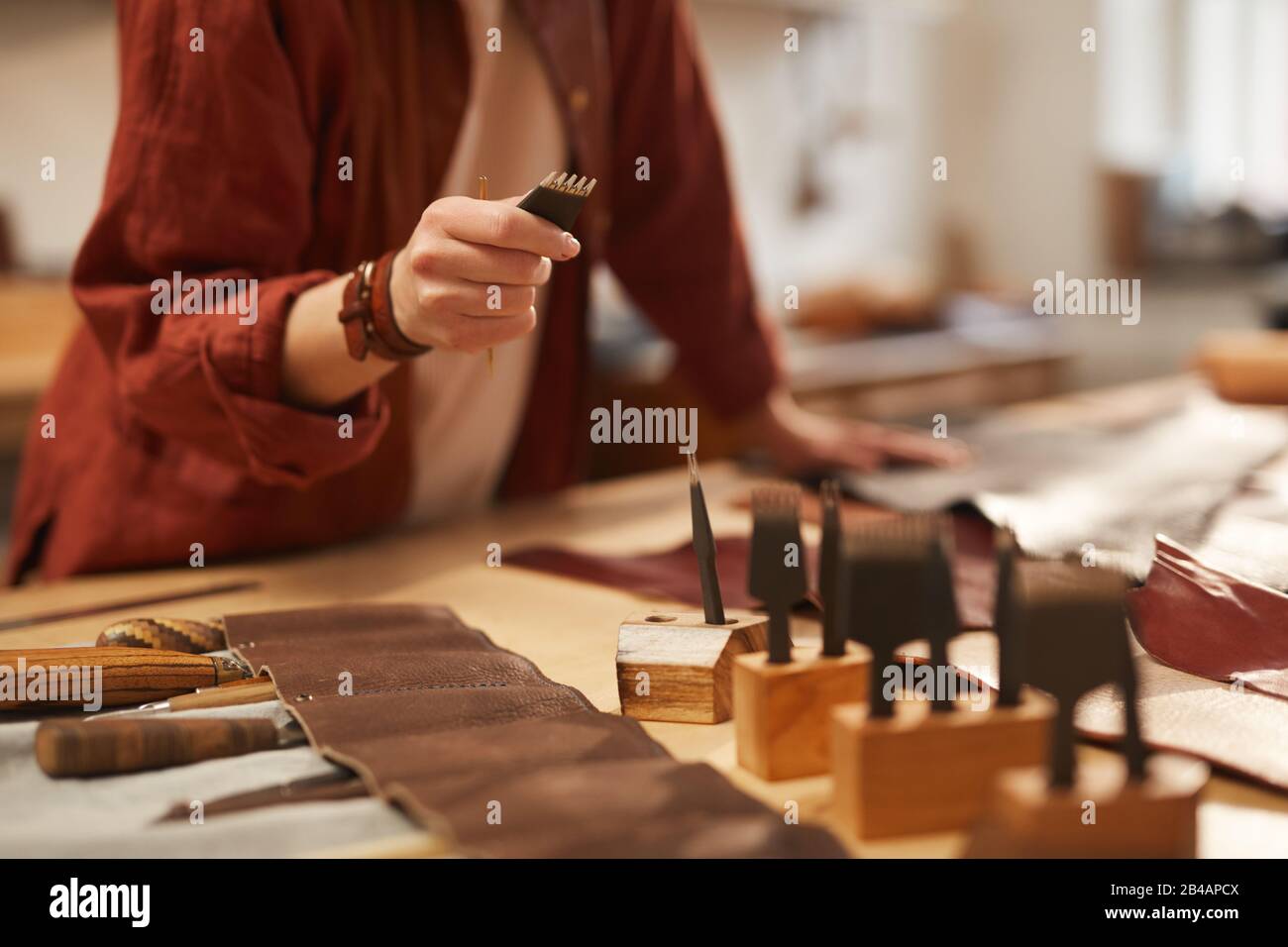 Unerkennbare Handwerkerin, die das richtige Werkzeug für die weitere Arbeit mit Leder und horizontalem Schuss wählt Stockfoto