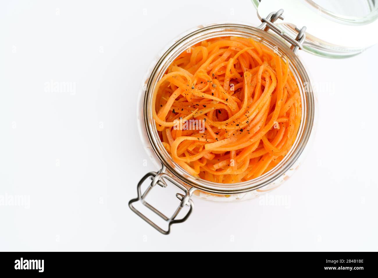 500 Gramm würziger koreanischer Karottensalat mit Öl, Knoblauch und schwarzem Pfeffer im Glasbecher. Nachhaltige Verpackung, weißer Hintergrund, hohe Auflösung Stockfoto
