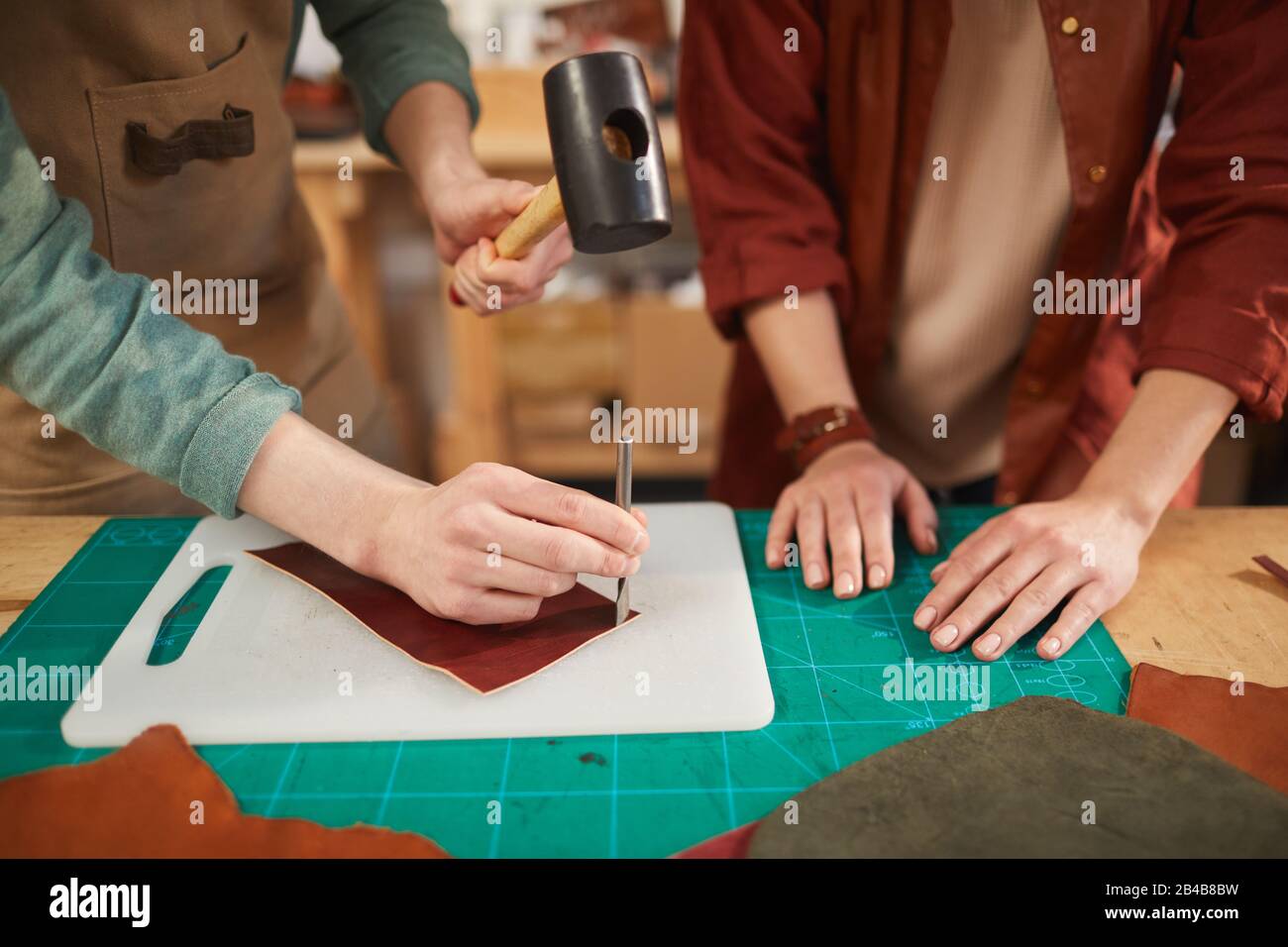 Hände von nicht erkennbaren Männern und Frauen, die in der modernen Lederhandwerkswerkstatt zusammenarbeiten, Kopierraum Stockfoto