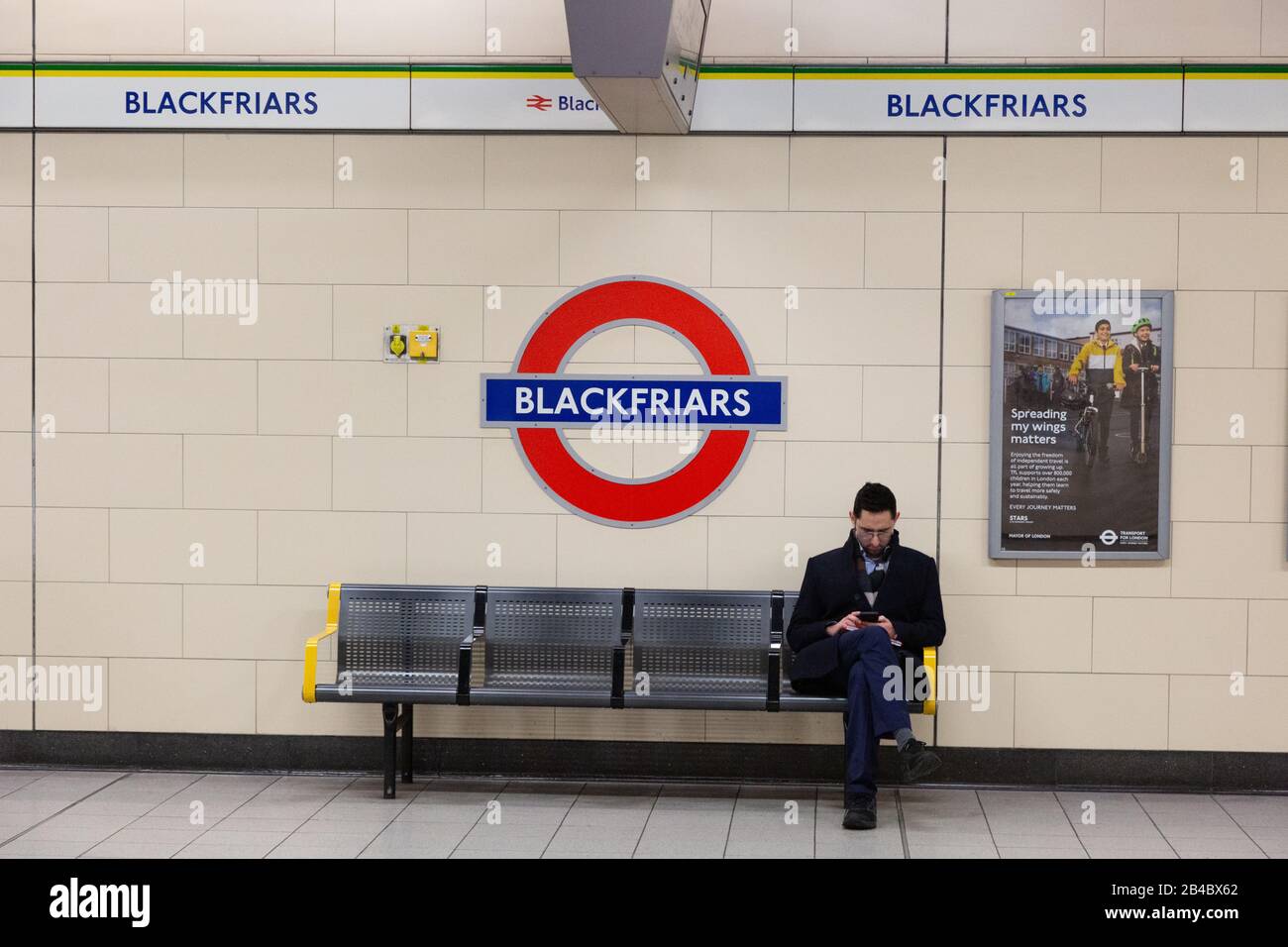 Ein Mann, der auf einer Bank auf der Plattform der Blackfriars U-Bahn-Station sitzt, oder Blackfriars London Underground Station, Blackfriars London UK Stockfoto