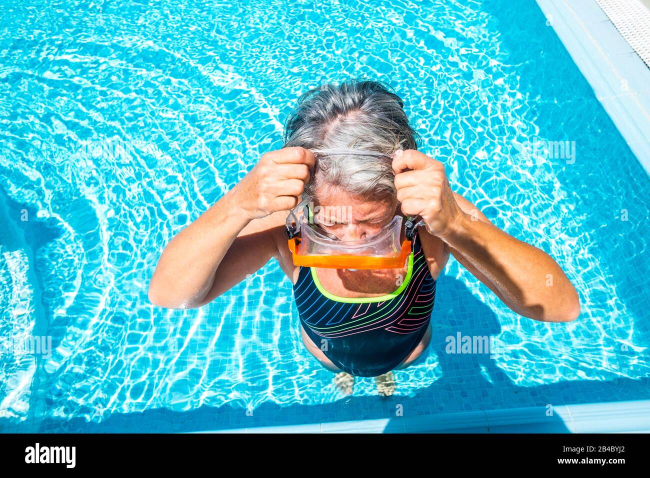 Silver Society alte aktive Frau nimmt Tauchmaske zum Schwimmen im Schwimmbad und genießt die Sommerzeit in klarem blauem Wasser - gesunder Lebensstil für Rentner im Freien Stockfoto