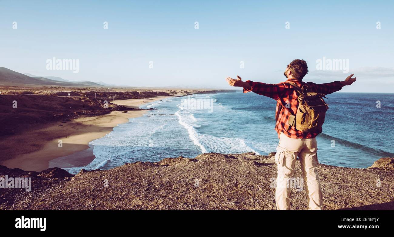 Der stehende Mann fühlt die Natur im Freien, die Arme vor einem wilden schönen Strand von der Spitze einer Klippe öffnet - alternativer Rucksackurlaub für Flusspferde Stockfoto Der stehende Mann fühlt die Natur im Freien, die Arme vor einem wilden schönen Strand von der Spitze einer Klippe öffnet - alternativer Rucksackurlaub für Flusspferde Stockfoto