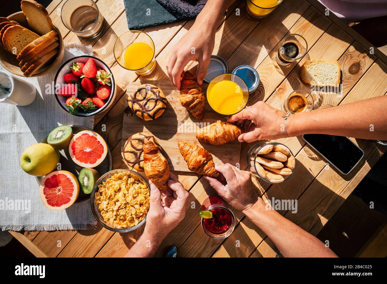 Luftansicht des Holzdesignttisches mit Speisen und Getränken zum Frühstück mit Freunden oder Familie zusammen - Freundschafts- und Zusammengehörigkeitskonzept mit Händen, die Bestechungen von einem Teller nehmen - oben vertikal Stockfoto