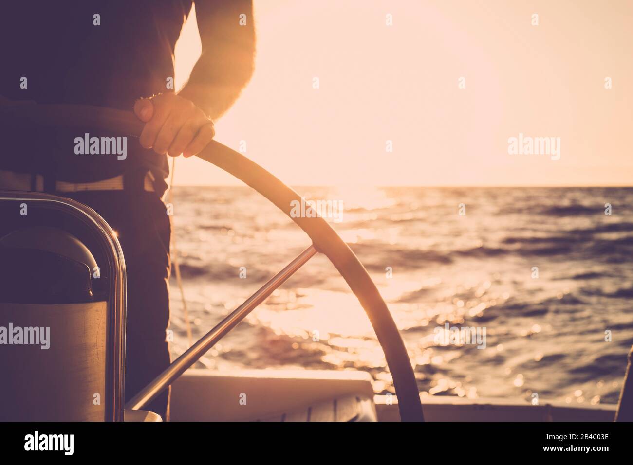 Nahaufnahme der Hand des Menschen auf dem Segelboothelm - Lifestyle-Konzept des Schiffs für schöne Urlaubsdestination - alternatives Menschenleben - Sonnenuntergang und Sonnenlicht im Hintergrund auf dem Ozean Stockfoto