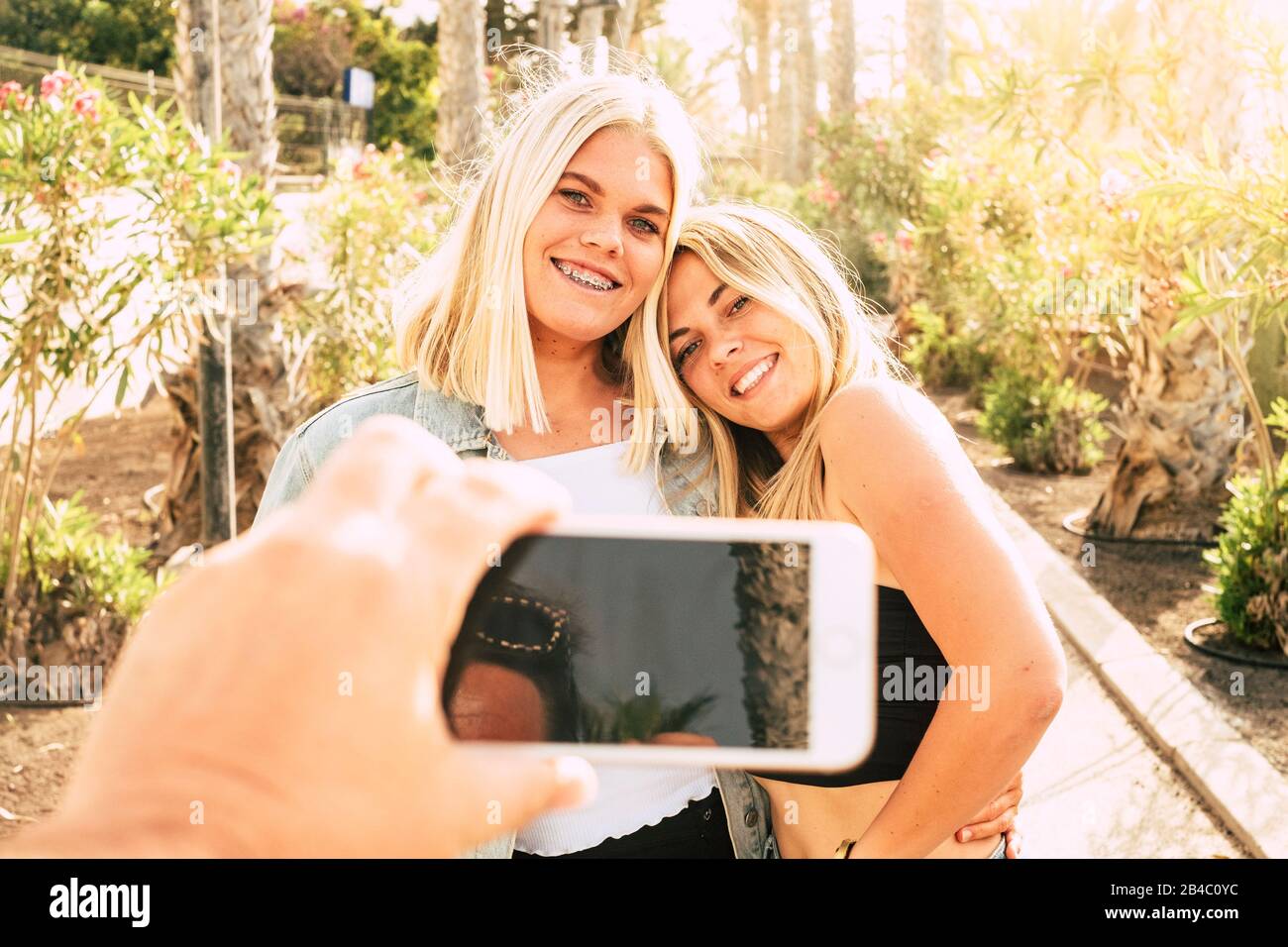 Fröhliche schöne Menschen Paar blonde Mädchen zusammen genießen die Outdoor-Freizeitaktivität an einem sonnigen Tag machen ein Bild von einem Freiling mit Handy zu teilen auf internete soziale Medien - Sonnenbeleuchtung Stockfoto