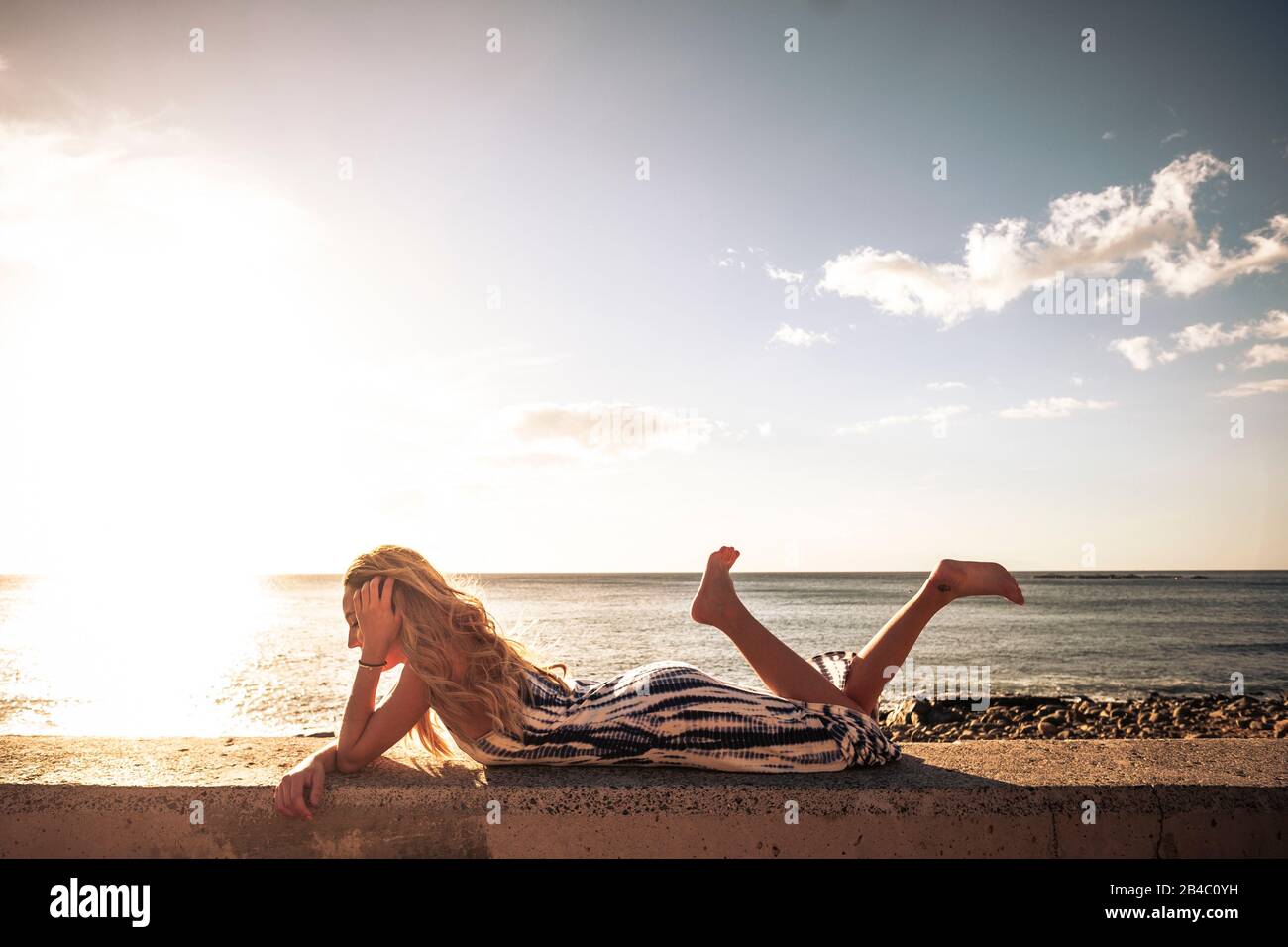 Schöne lange blonde Haare junge Frau legt sich auf und genießt den Sonnenuntergang am Meer - unabhängige Mädchen mit Meer und Sonnenlicht Sonnenuntergang im Hintergrund - genießen Sie Freiheit und Sommerurlaub Stockfoto