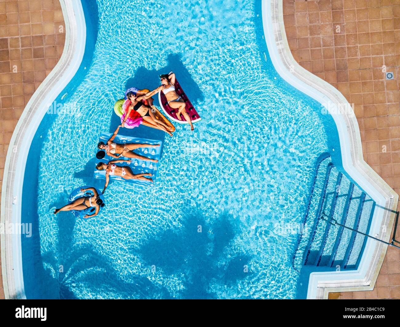 Farbenfroher Lufthintergrund mit einer Gruppe von Freunden kaukasische Menschen genießen den Sommerurlaub am blauen Wasserpool mit angesagten aufblasbaren Matratzenlilos zusammen mit Spaß und Glück Stockfoto