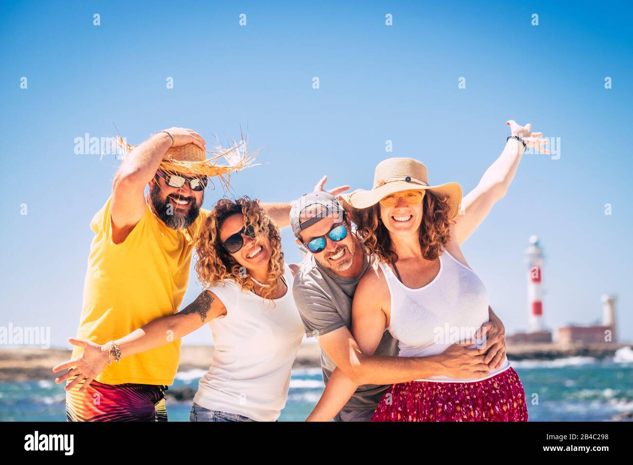 Eine Gruppe glücklicher Menschen und fröhlicher Erwachsener, die zusammen während des Sommerurlaubs am Strand Spaß haben - den Strand und das Meer im Freien genießen - blauer Himmel und Leuchtturm im Hintergrund Stockfoto