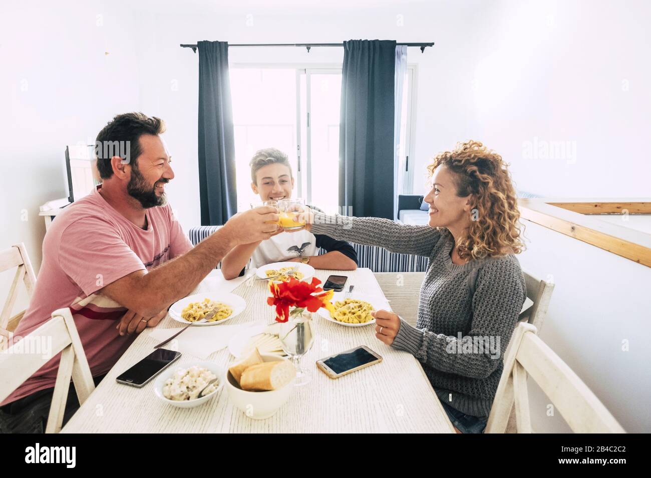 Glückliche Menschen kaukasische Familie mit Papa und Sohn vereinen sich zu Hause in einem weißen hellen Raum - gewöhnliches reales Leben für fröhliches Paar mit Teenager - Mobiltelefontechnologie Stockfoto