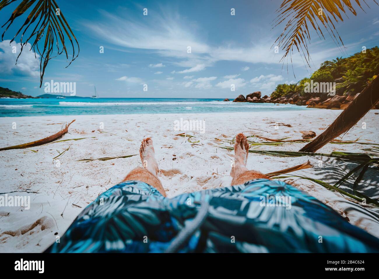 POV-shot von Mensch tragen blaue Badeshorts Festlegung auf einem schönen Sandstrand Cosos tropischen Strand Anse, La Digue, Seychellen. Stockfoto