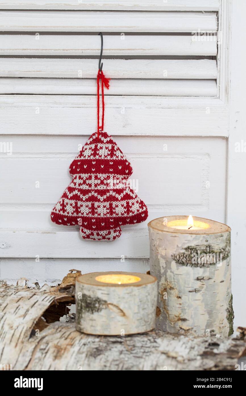 Rustikales Weihnachtsleben nordischer Stil mit Birkenkerze und niedlichem Strickweihnachtsbaum, der an einer weißen Verschlusstür hängt Stockfoto