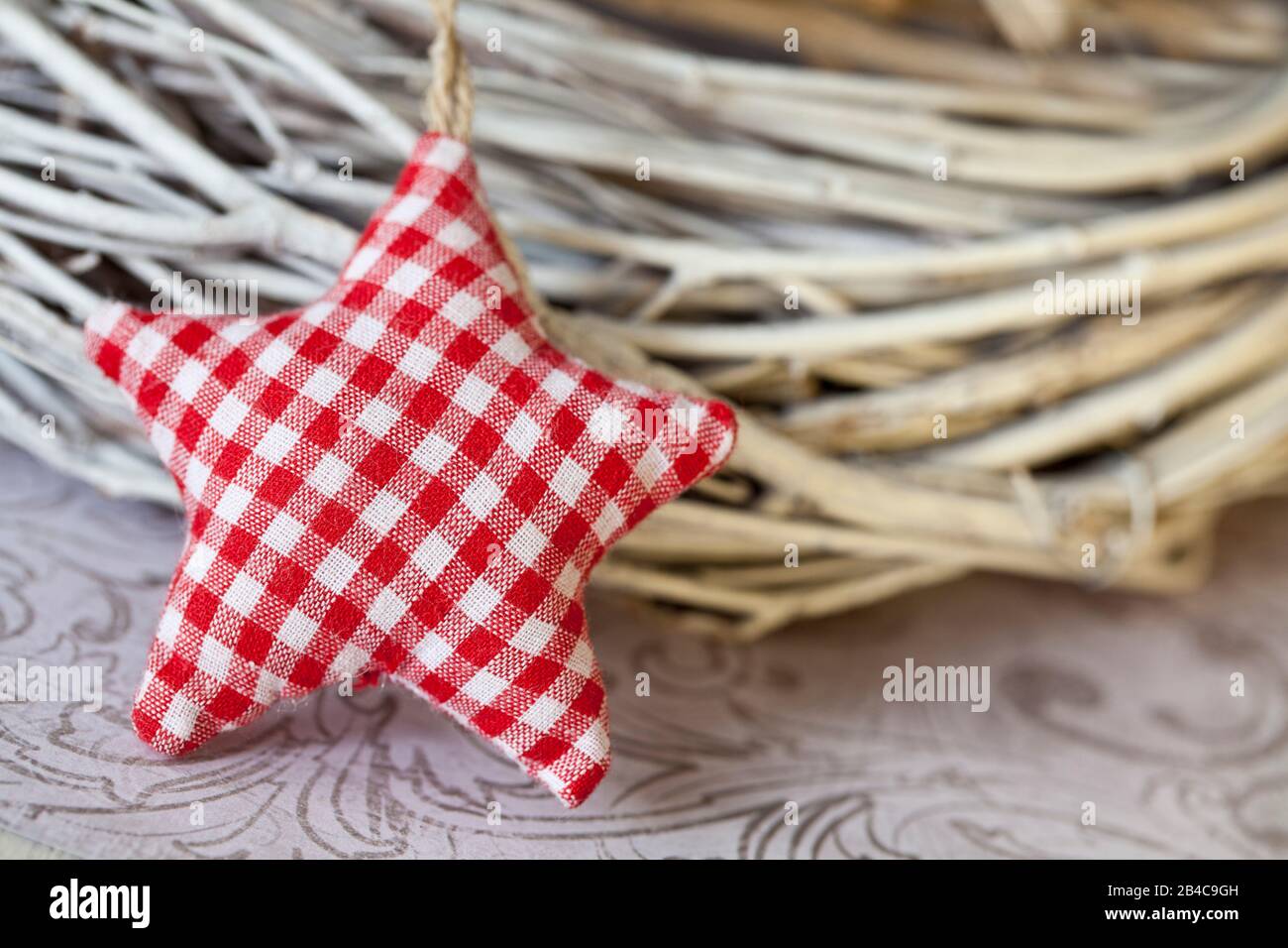 Nordisches Weihnachtsleben mit rot-weißem Gingham Textilstern, der sich auf Korbkranz neigt Stockfoto