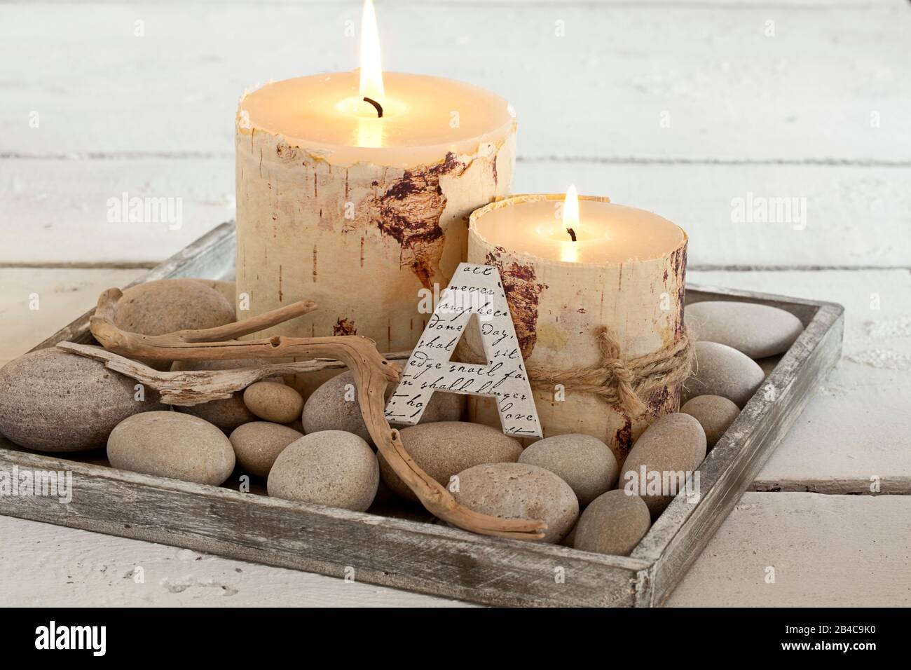 Rustikales Weihnachts- oder Herbststillleben mit Kerzen im Birkenrindenstil, Buchstaben A und Treibholz auf einem Teller mit Kieselstein Stockfoto