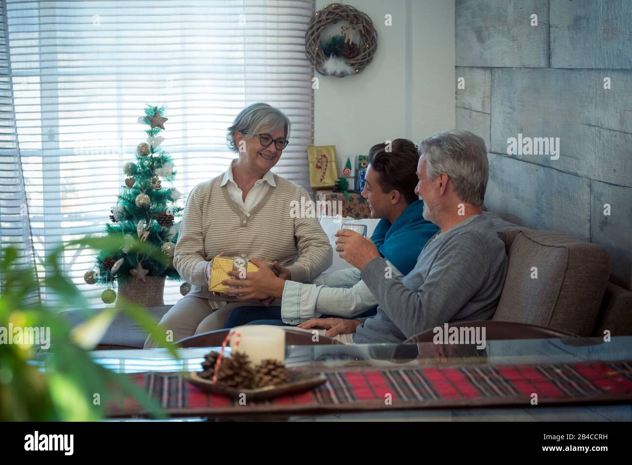 Familie mit gemischten Generationen von jung bis Senior feiern weihnachten zu Hause mit Freude und Liebe - Großväter und Enkel sitzen auf dem Sofa mit Geschenken und Geschenken Stockfoto