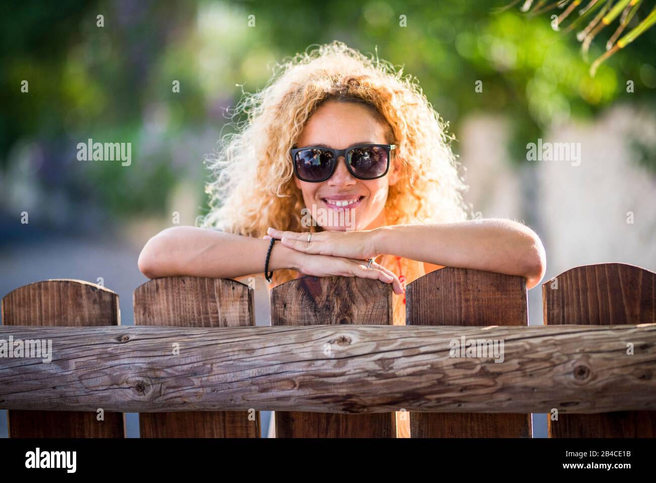 Porträt einer schönen fröhlichen fröhlichen Frau mit Sonne in Hintergrundbeleuchtung und einem schönen Lächeln mit Blick auf die Kamera - grüner Naturhintergrund - genießen Sie die Freizeitgestaltung im Freien auf dem Land Stockfoto