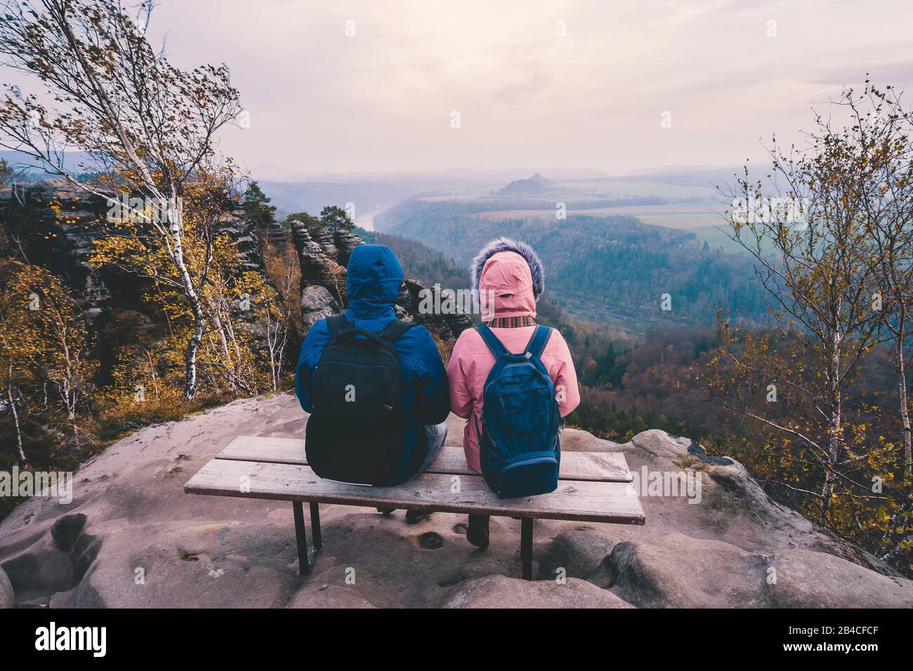 Junges Paar im winterlichen Kleidungs mit Rucksäcken, die nach der Wanderung auf einem Kalksteinfelsen sitzend die Ansicht der Landschaft genießt, Reise-Li Stockfoto